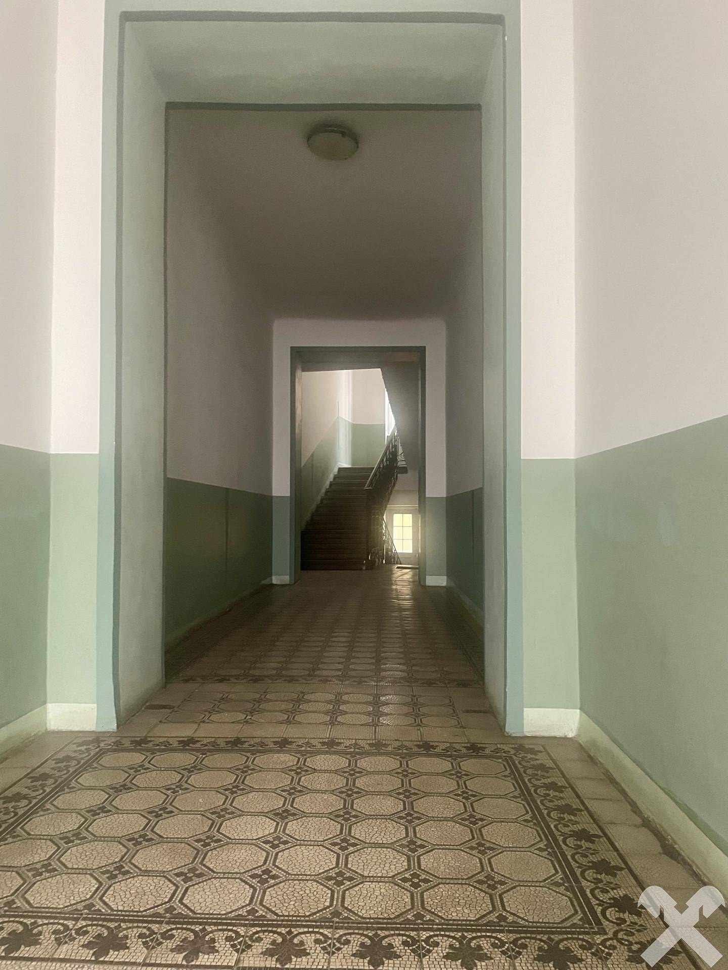 Langer Flur mit gemusterten Fliesen und Treppenaufgang in einem Altbau mit natürlichem Licht.