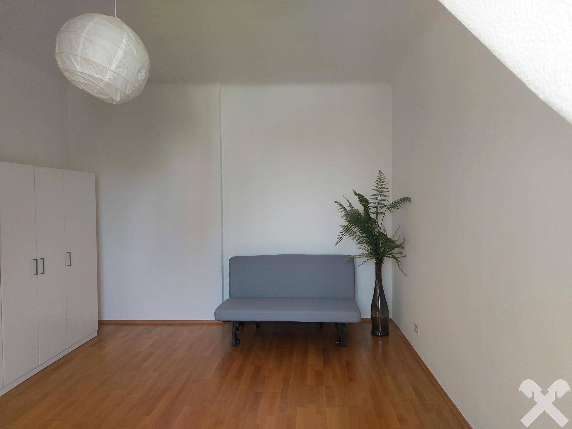 Heller Raum mit Dachschräge, Holzfußboden und einfacher Einrichtung, ideal als Schlafzimmer.