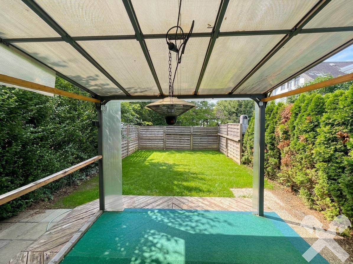 Blick von der überdachten Terrasse auf den privaten Gartenbereich mit Rasen und Holzzaun.