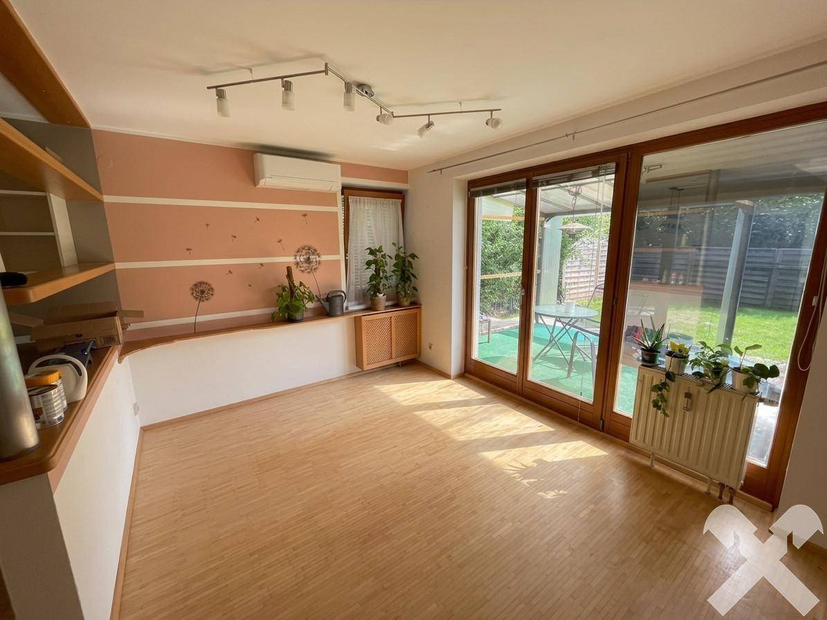 Helles Wohnzimmer mit Holzboden, großen Schiebetüren zum Garten und Klimaanlage.