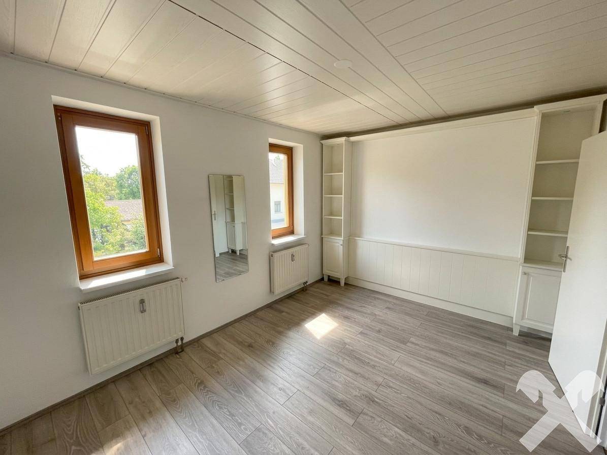Helles Schlafzimmer mit Laminatboden, weißen Wänden und Einbauregalen.