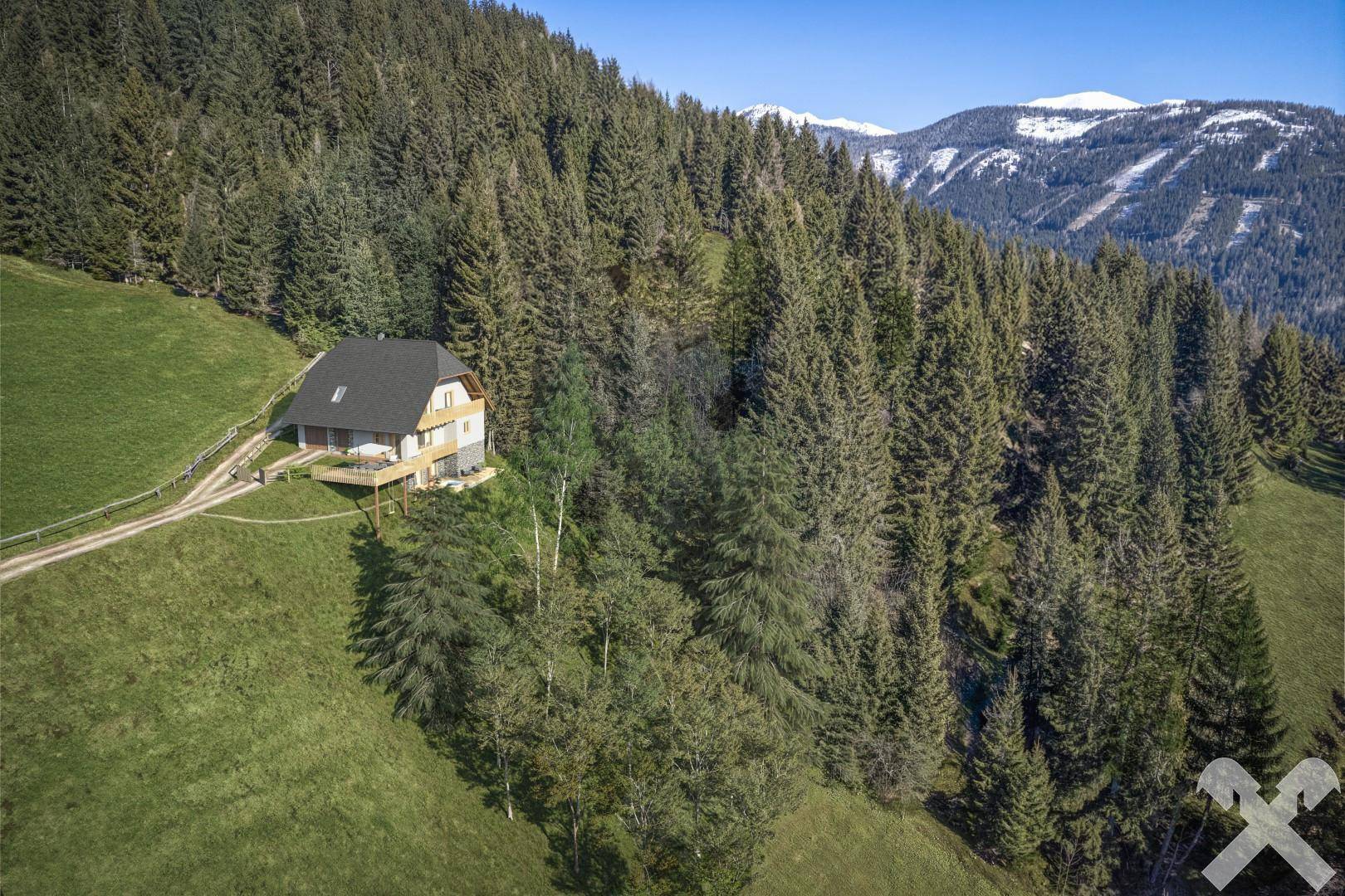 Luftaufnahme des Hauses inmitten einer bewaldeten Berglandschaft mit schneebedeckten Gipfeln.