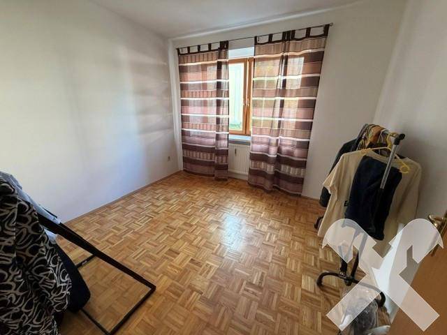 Schlafzimmer mit Parkettboden, einem Fenster mit gestreiften Vorhängen und ausreichend Tageslicht.