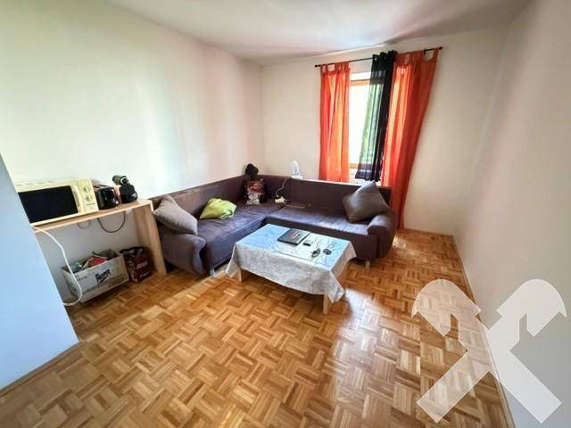 Gemütliches Wohnzimmer mit L-förmigem Sofa, Parkettboden und farbigen Vorhängen am Fenster.