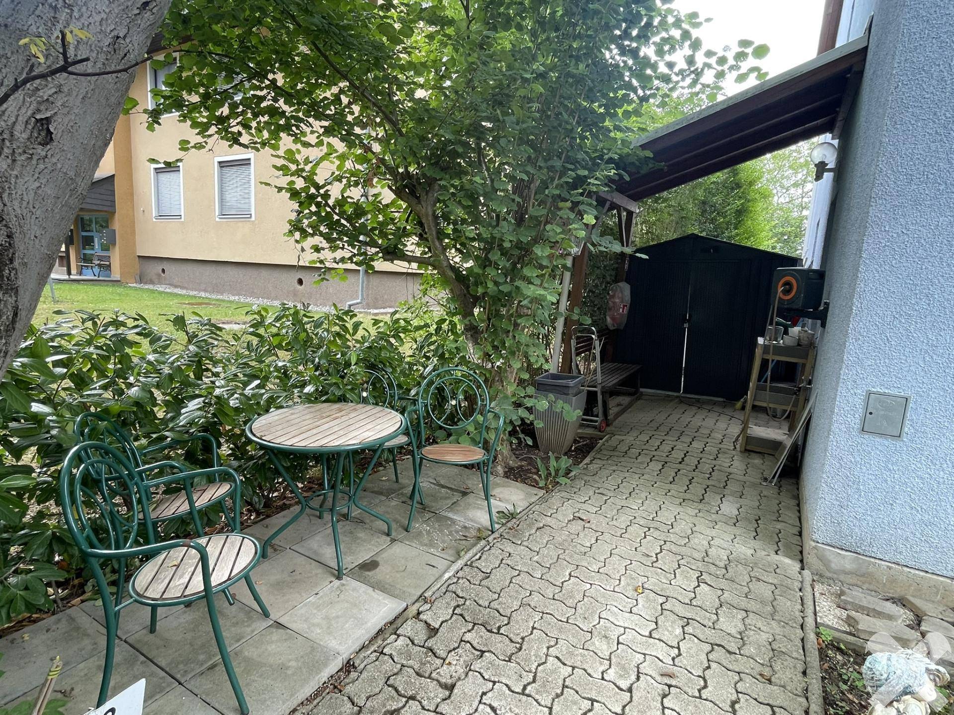 Gemütlicher Außenbereich mit Gartentisch und Stühlen, umgeben von Bäumen und Sträuchern.