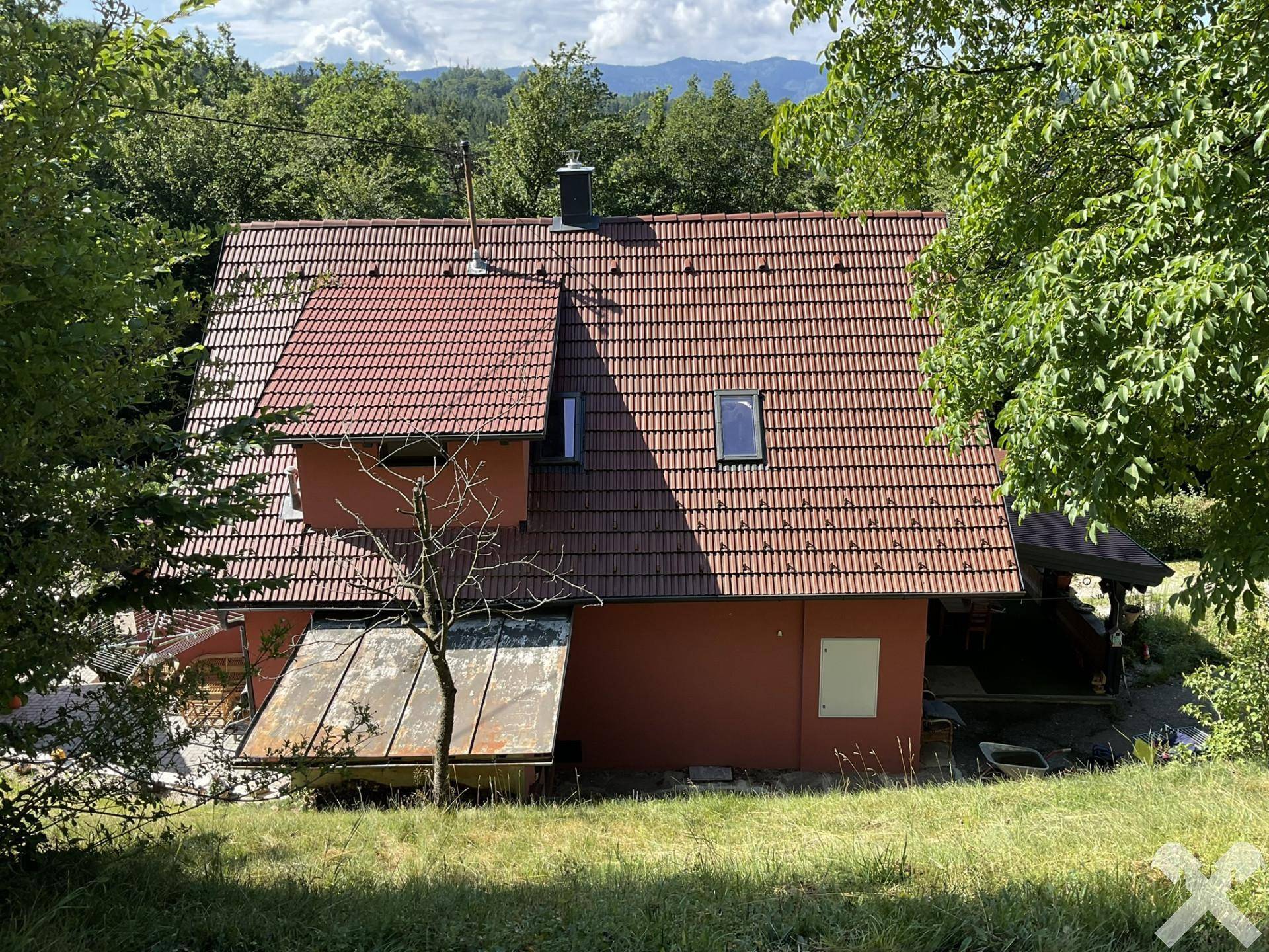 Rückansicht des roten Hauses mit braunem Ziegeldach, Dachfenstern und überdachtem Außenbereich.