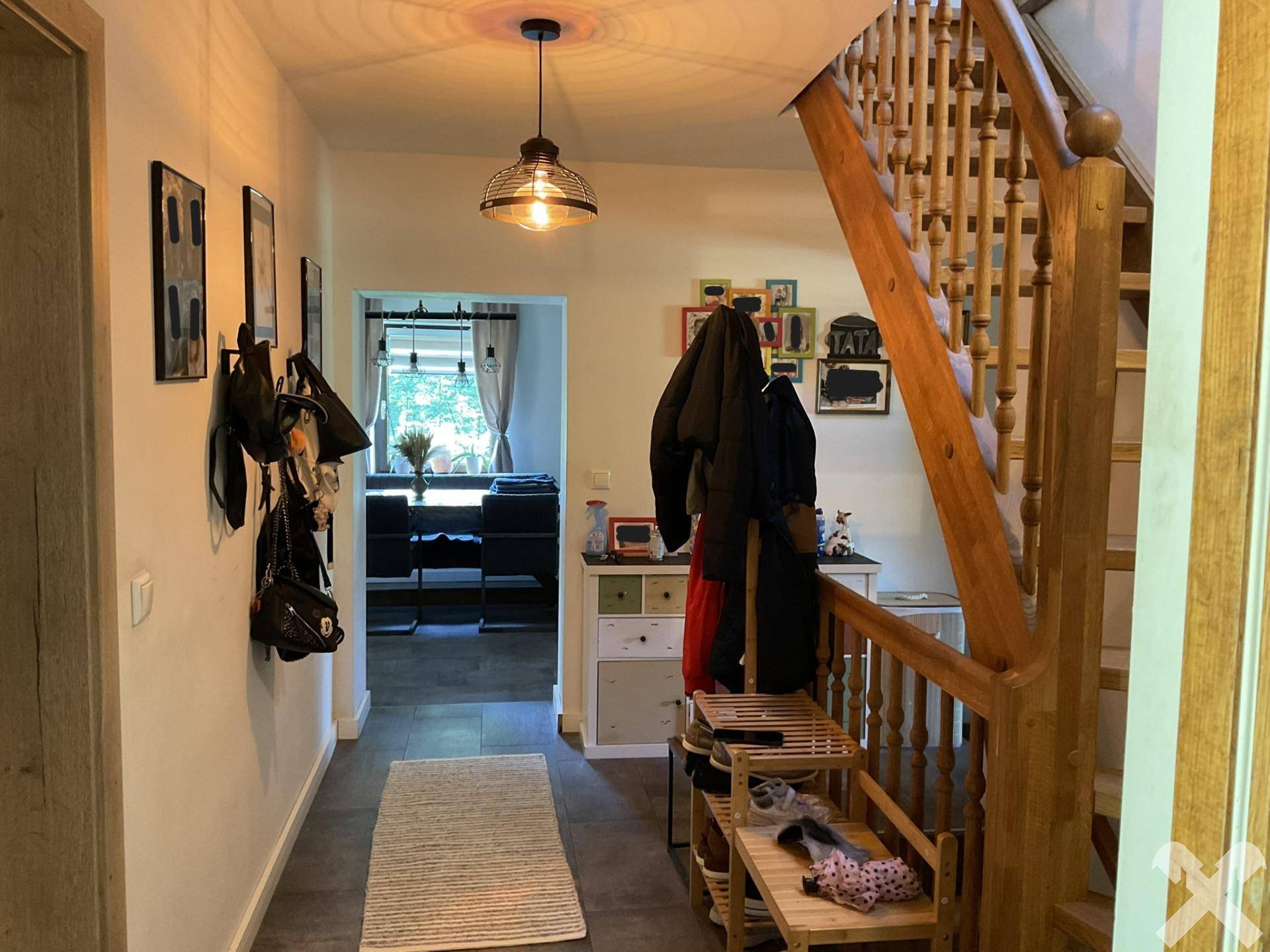 Heller Flur mit Holztreppe, gefliestem Boden und Garderobe, der zu weiteren Räumen führt.