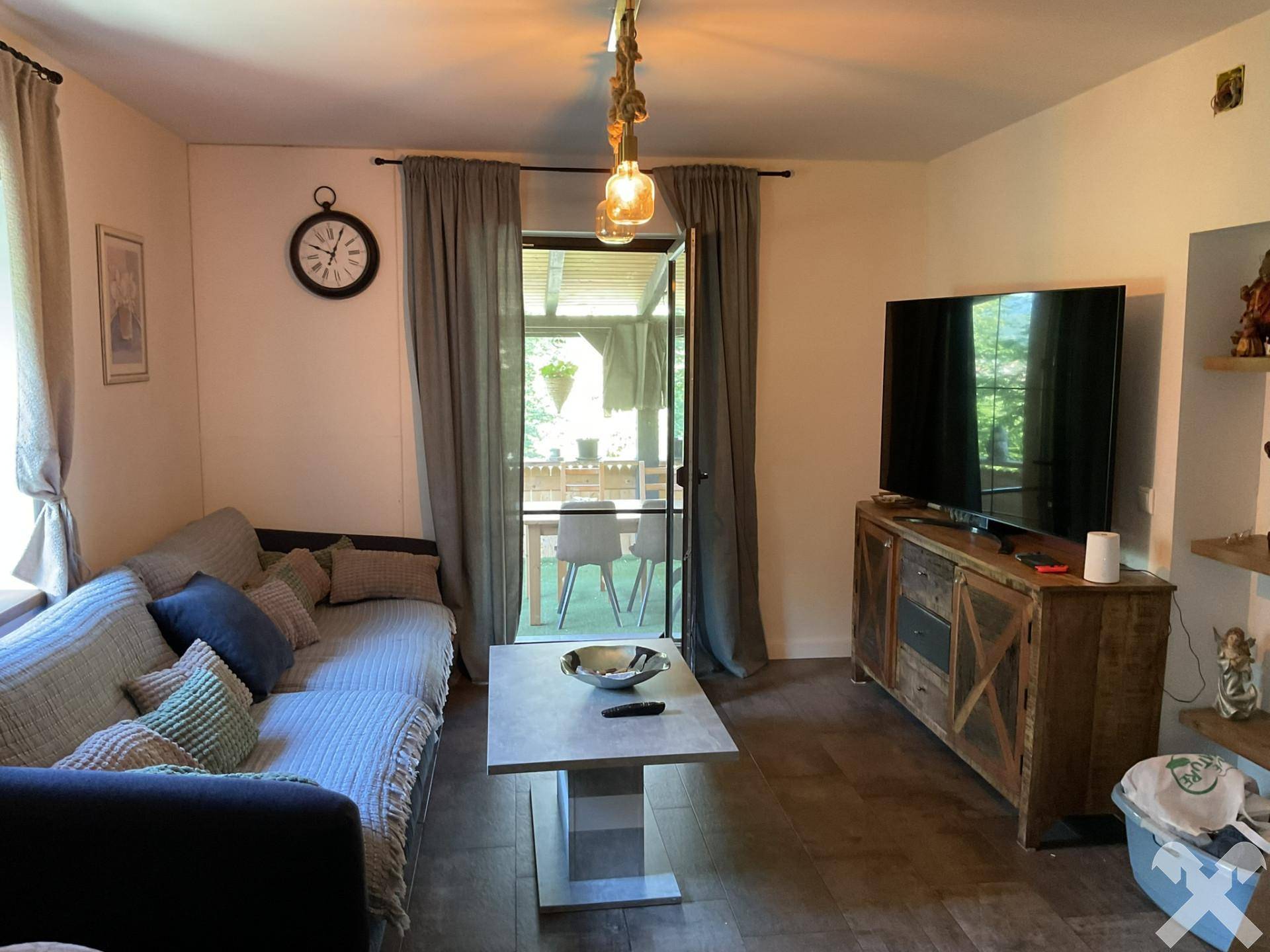 Gemütliches Wohnzimmer mit Sofa, Couchtisch und Fernseher, mit Zugang zu einem überdachten Außenbereich.