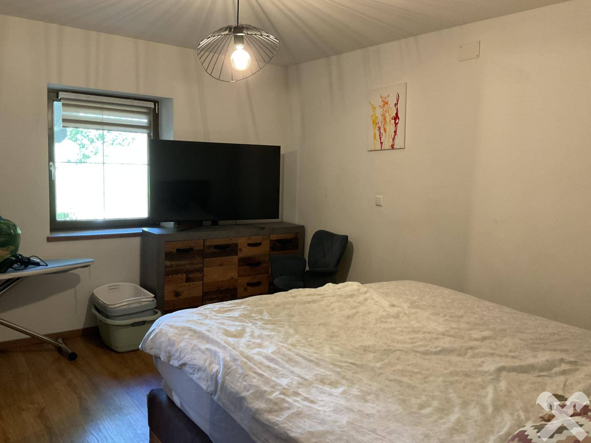 Schlafzimmer mit großem Bett, Fernseher auf einem Holzschrank und Fenster, ausgestattet mit Holzfußboden.