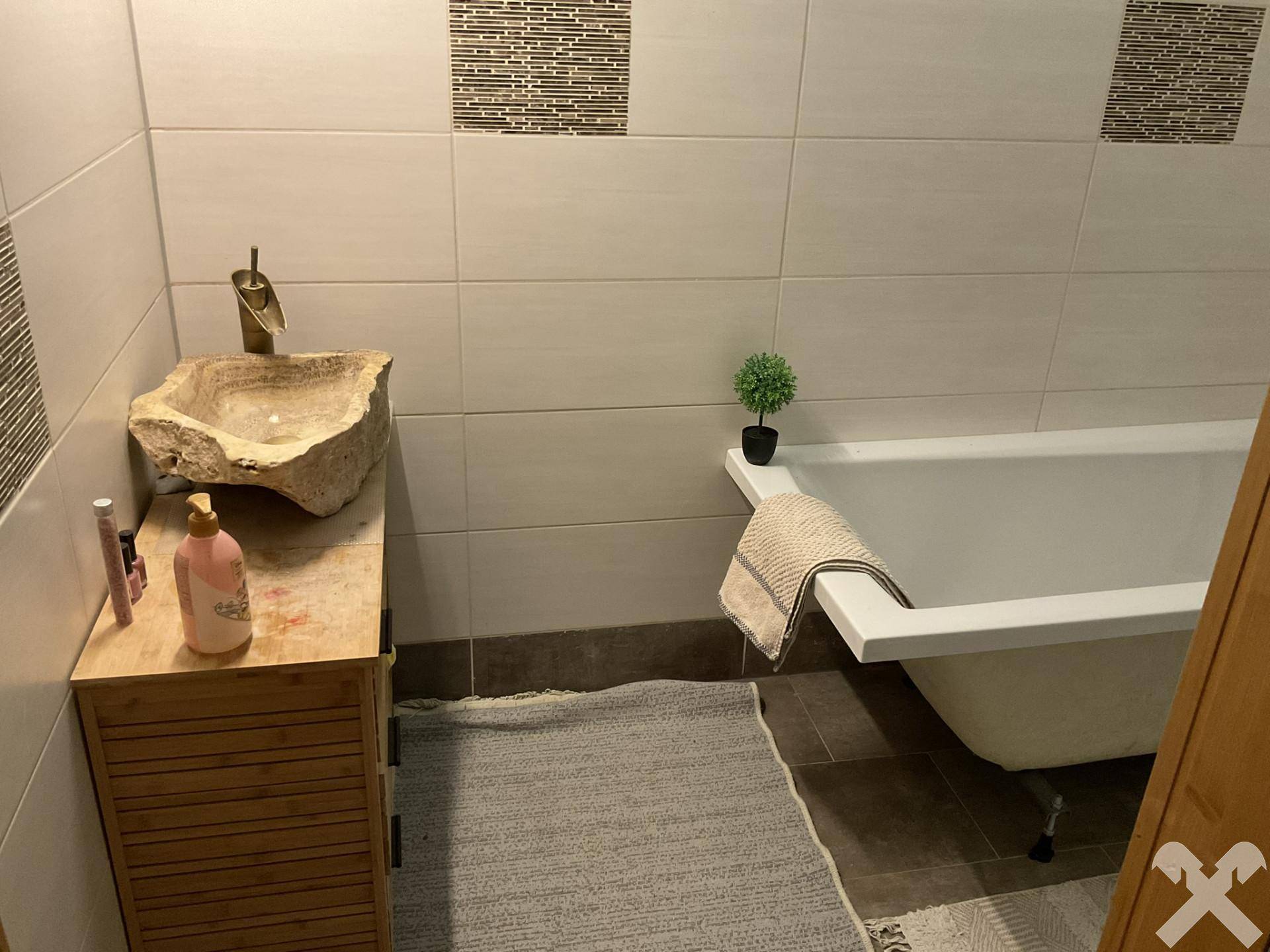 Badezimmer mit Badewanne, einzigartigem Steinwaschbecken auf Holzunterschrank und gefliesten Wänden.