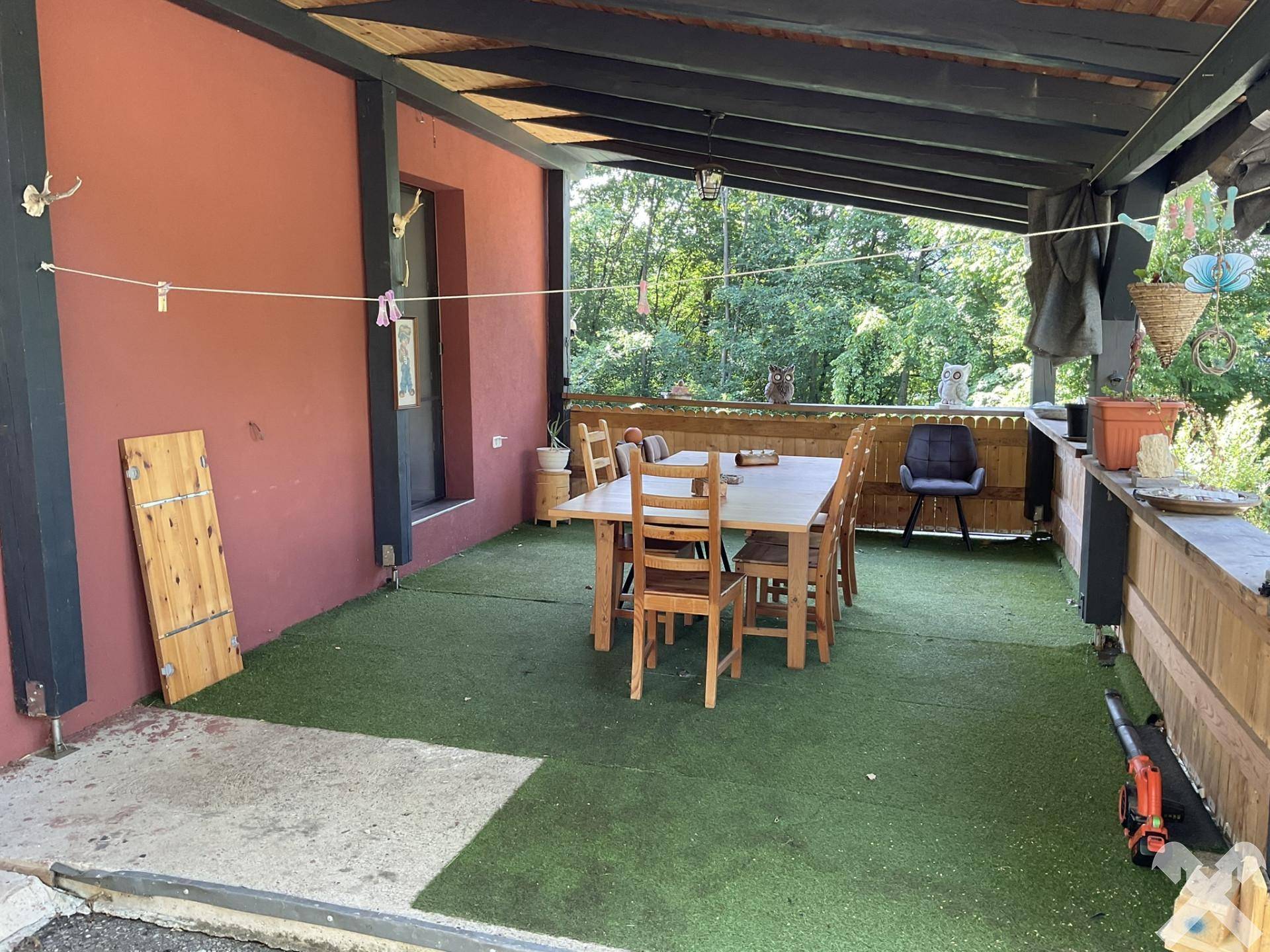 Überdachte Terrasse mit Esstisch und Stühlen, ausgelegt mit Kunstrasen für den Außenbereich.