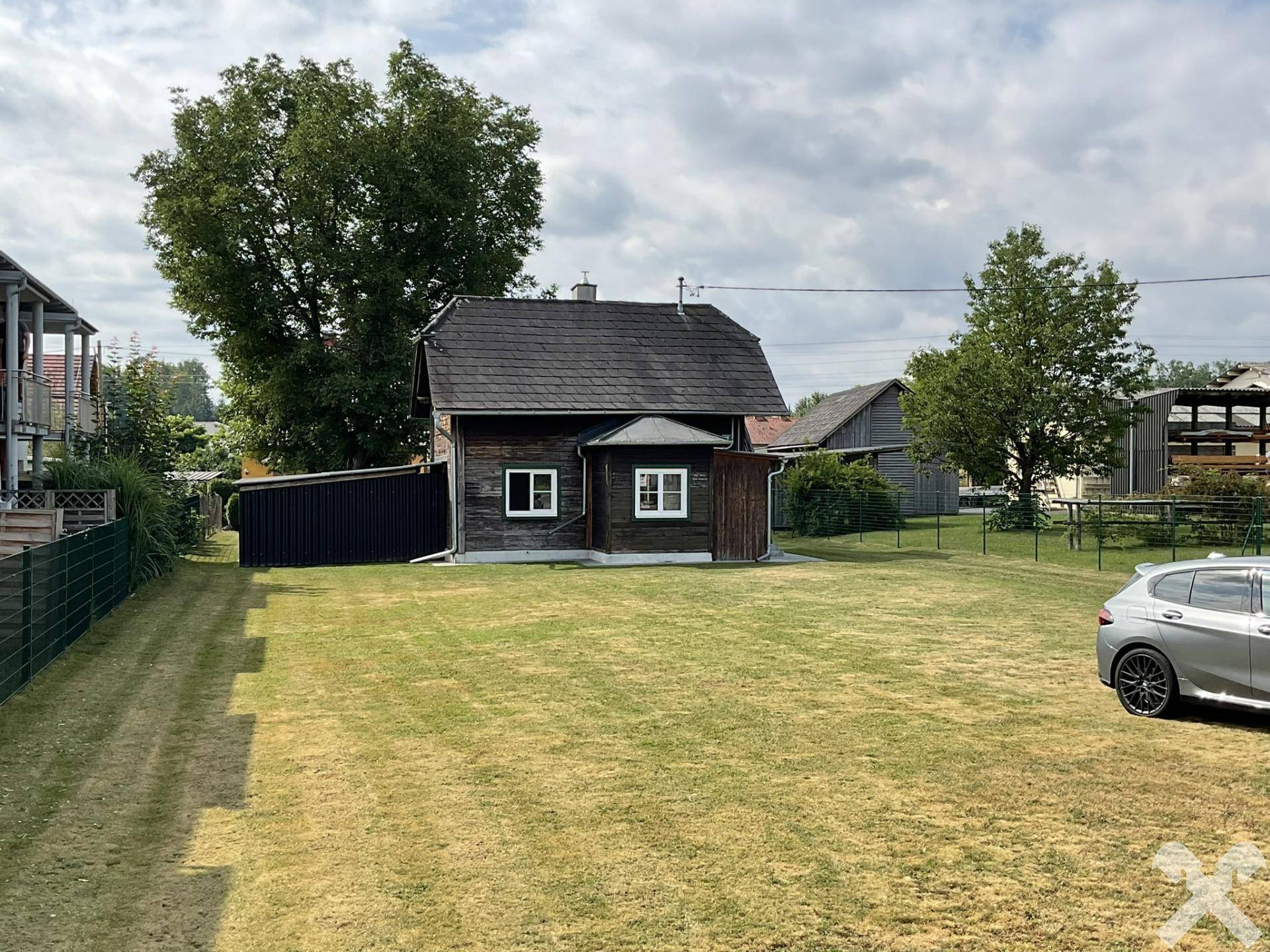 Weitläufiger Rasenbereich mit einem traditionellen Holzhaus und einem geparkten Auto am Rande des Grundstücks.