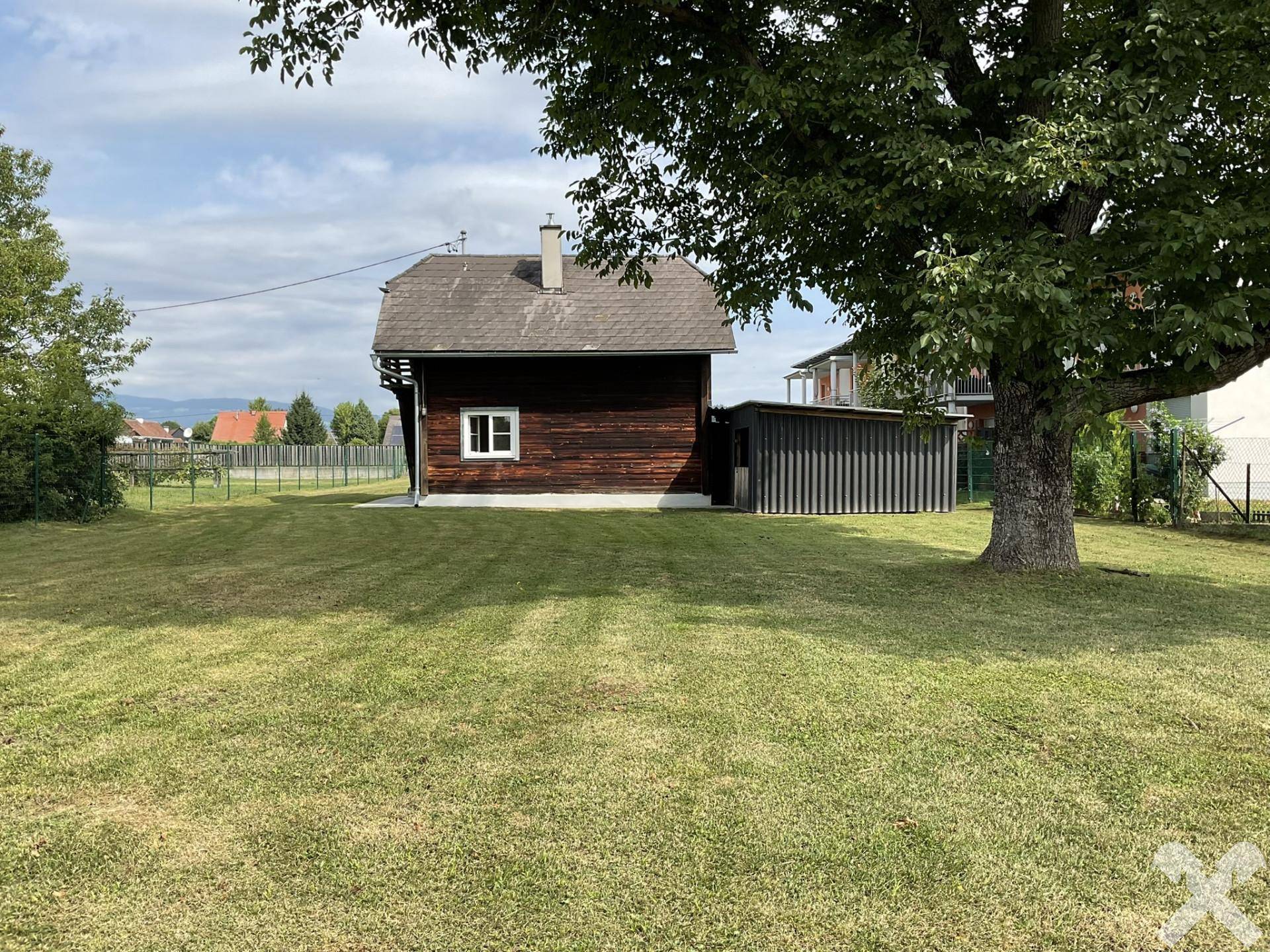 Blick auf das Holzhaus von der Rückseite, umgeben von einer weitläufigen Rasenfläche und einem großen Baum.