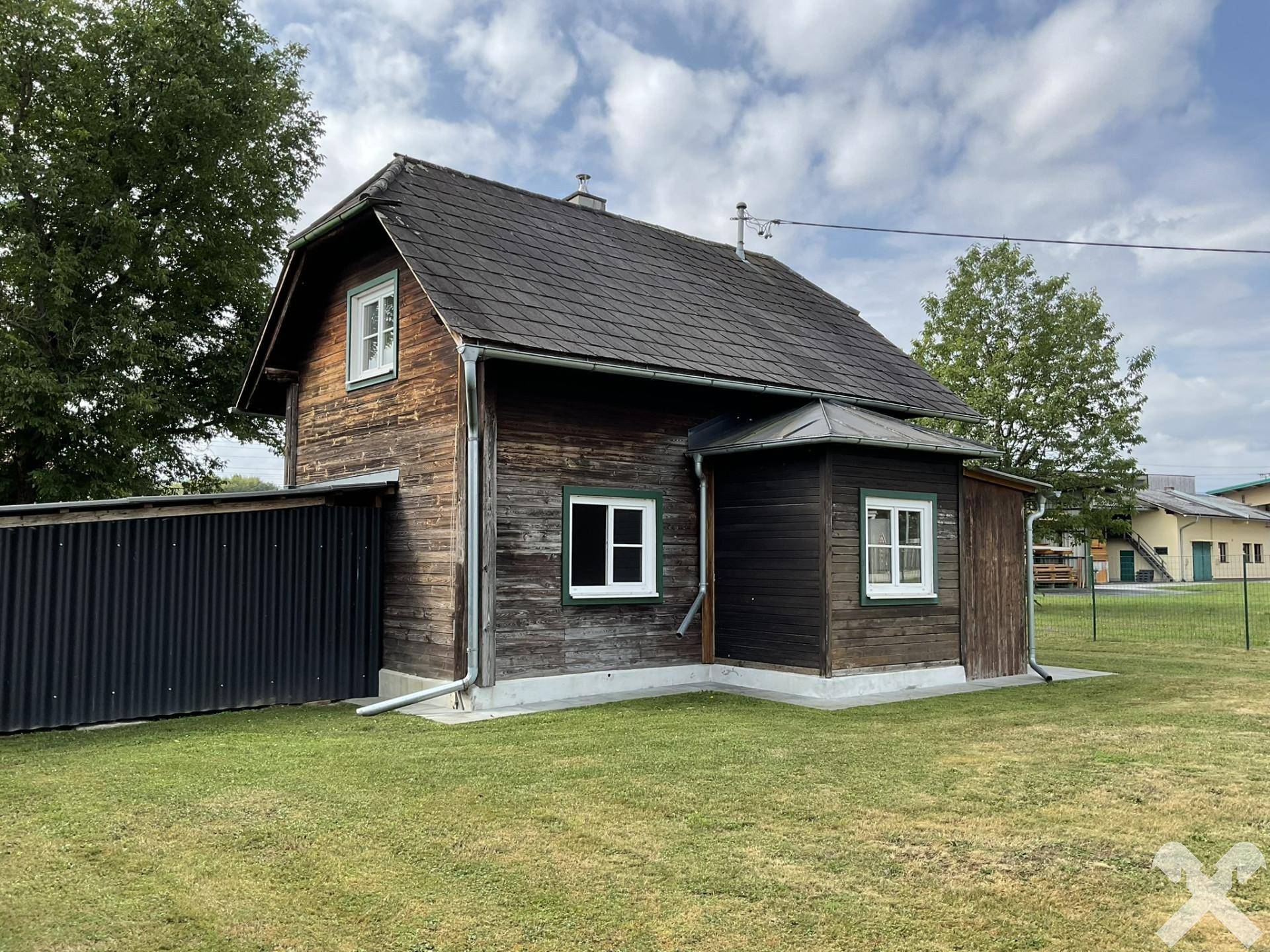 Traditionelles Holzhaus mit Satteldach und weißen Fenstern, umgeben von einer gepflegten Rasenfläche.