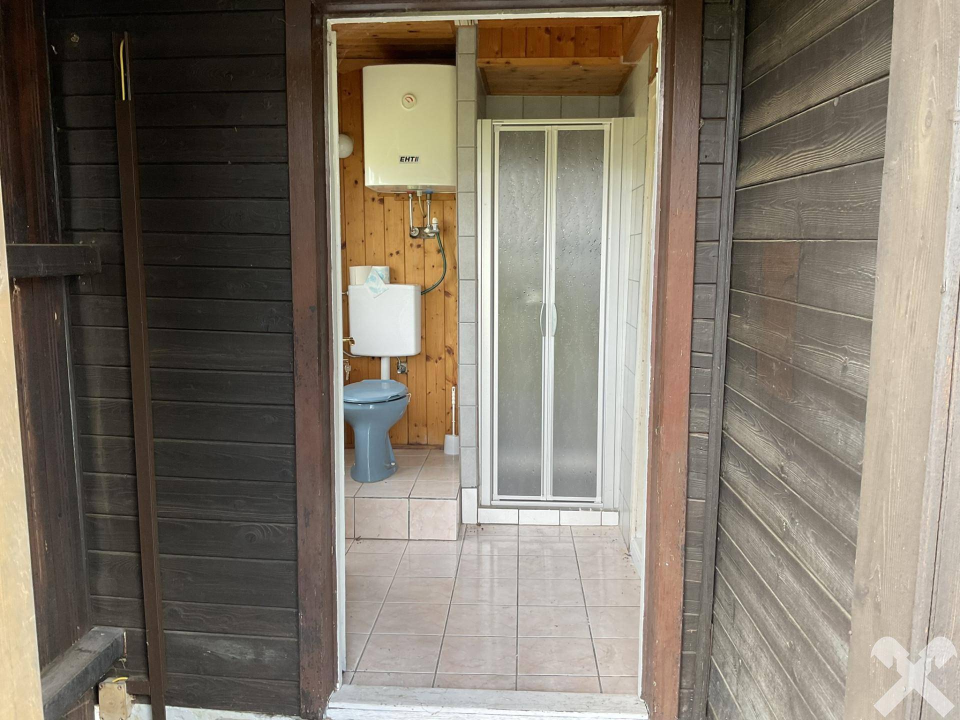 Kleines Badezimmer mit WC, Dusche und Holzverkleidung an den Wänden, einfach und funktional.