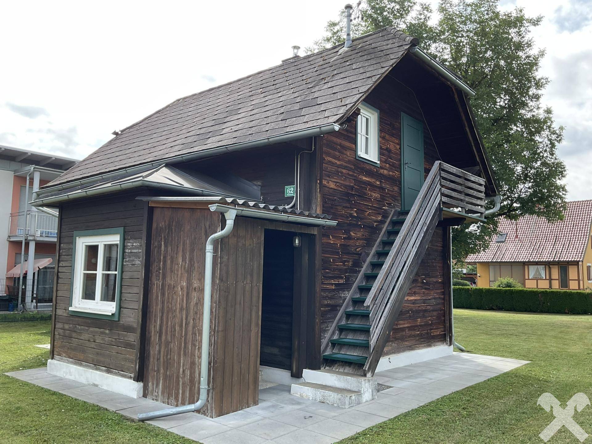 Charmantes Holzhaus mit Außentreppe zum oberen Stockwerk und einem kleinen Vordach über dem Eingang.