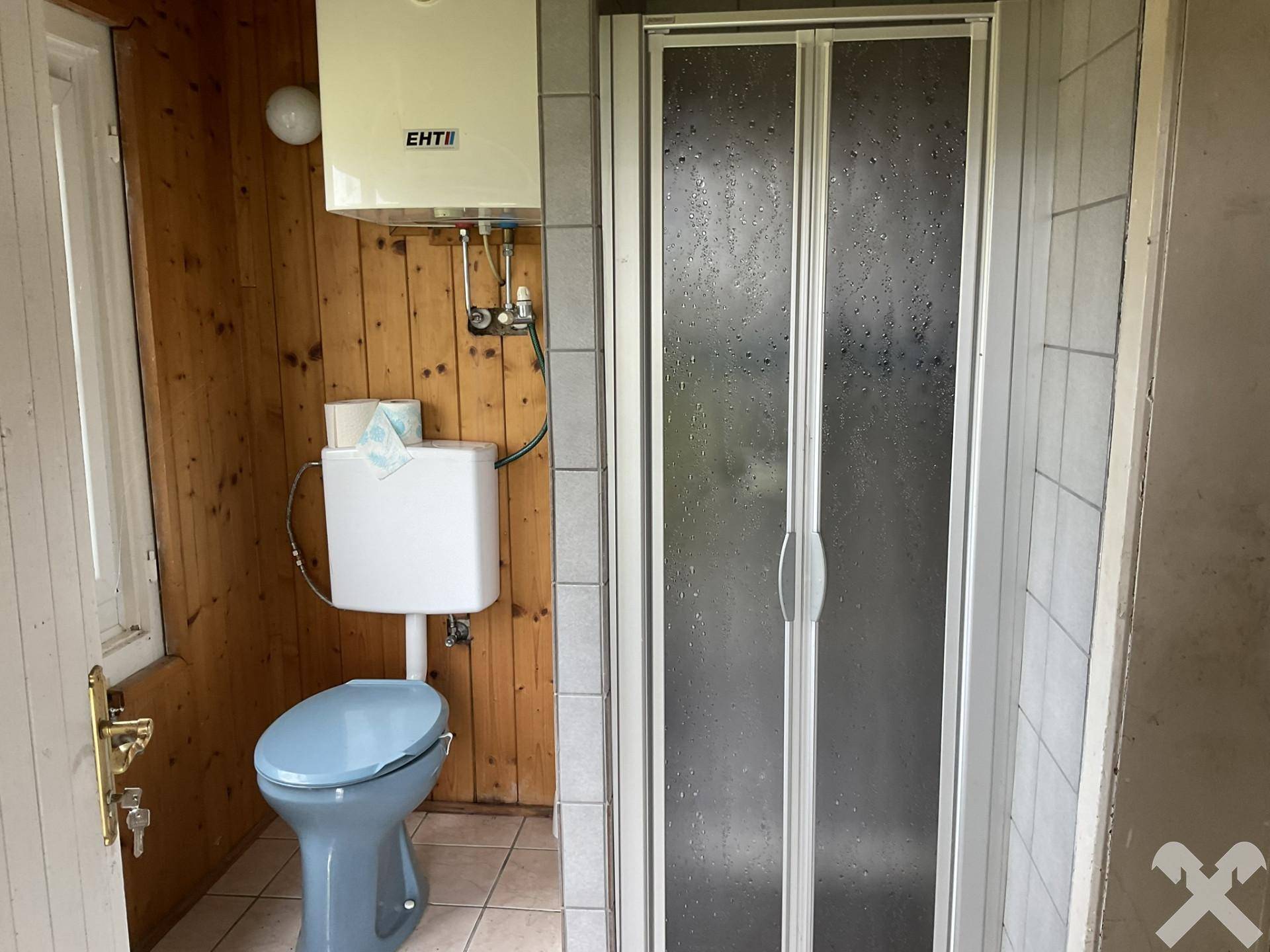 Funktionales Badezimmer mit blauer Toilette, Duschkabine und holzvertäfelten Wänden, einfach ausgestattet.
