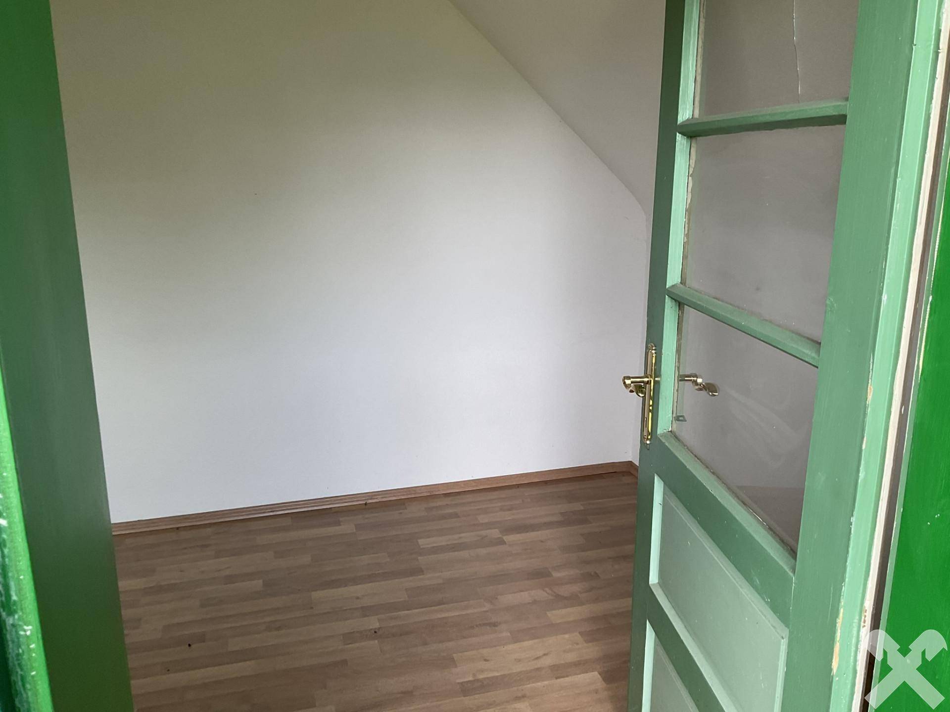 Dachzimmer mit Laminatboden und schrägen Wänden, durch eine grüne Tür zugänglich, bietet gemütlichen Raum.