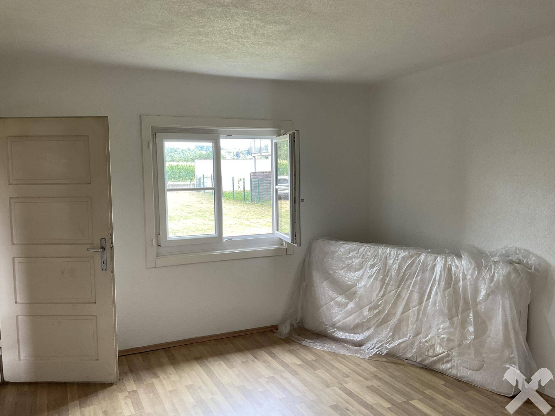 Helles Zimmer mit Laminatboden und einem Fenster, das einen Blick auf die Umgebung bietet.