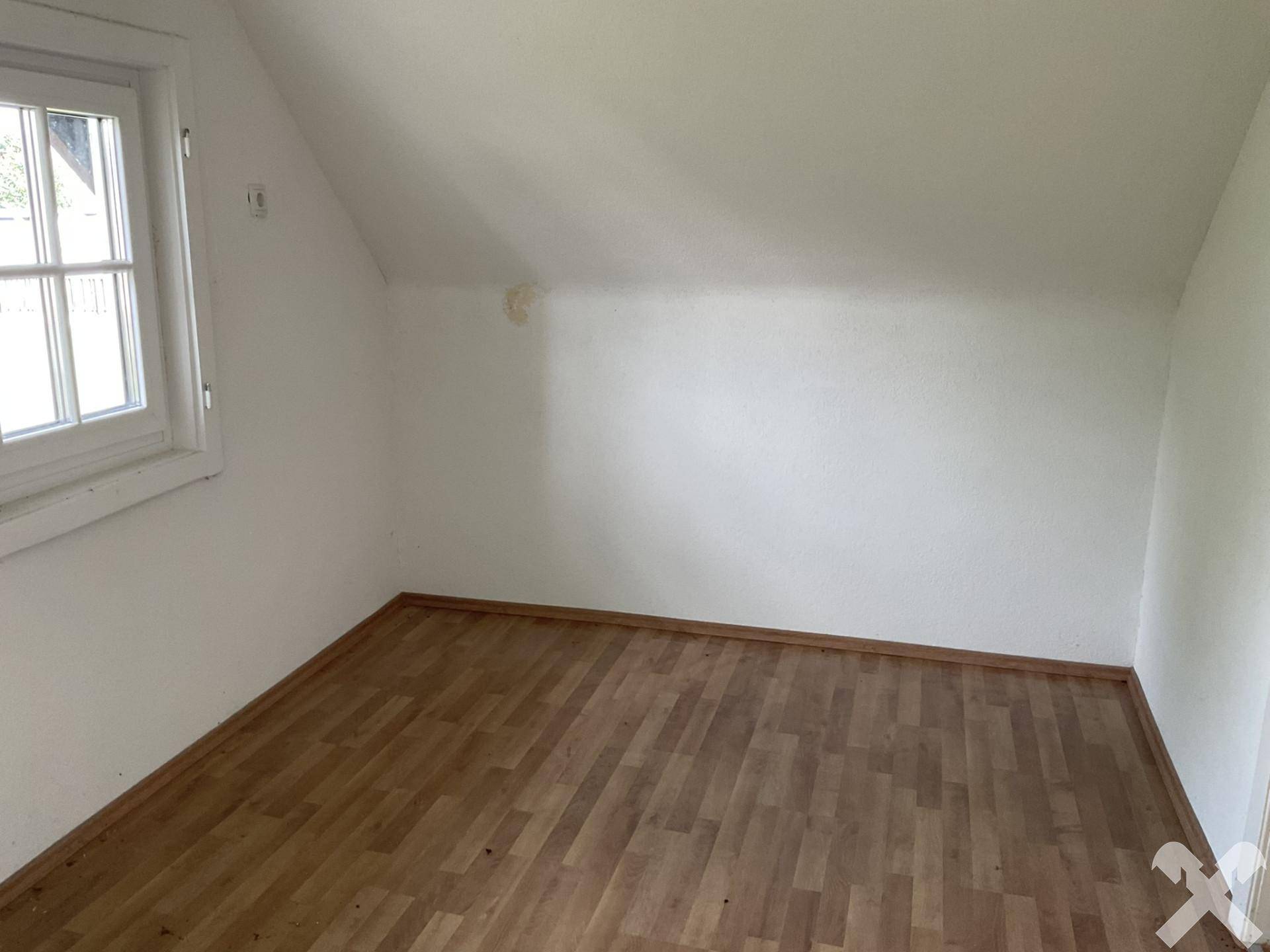 Gemütliches Dachzimmer mit Laminatboden und einem Fenster, das viel Tageslicht hereinlässt.