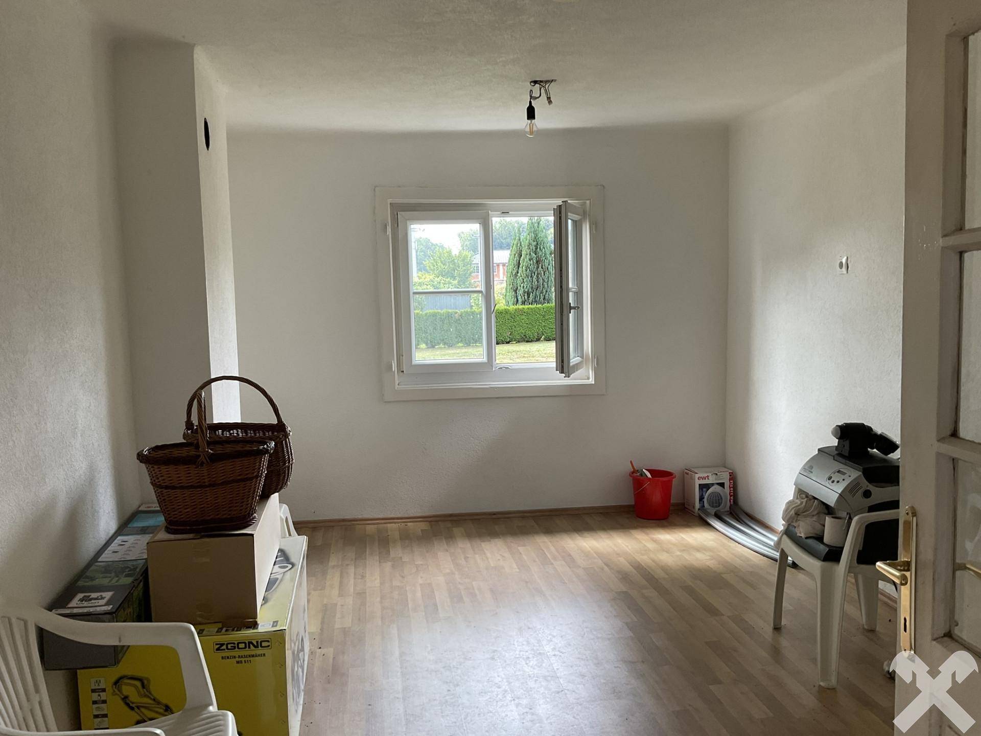 Helles Zimmer mit Laminatboden und einem Fenster mit Blick ins Grüne, derzeit als Abstellraum genutzt.