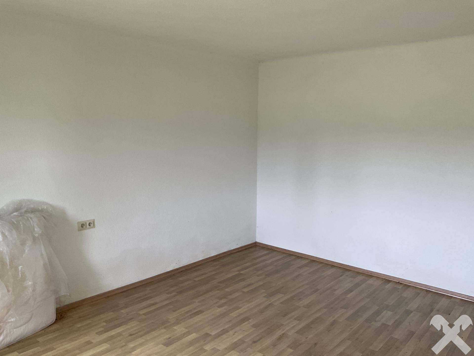 Leeres Zimmer mit weißen Wänden und Laminatboden, bereit für die individuelle Gestaltung.