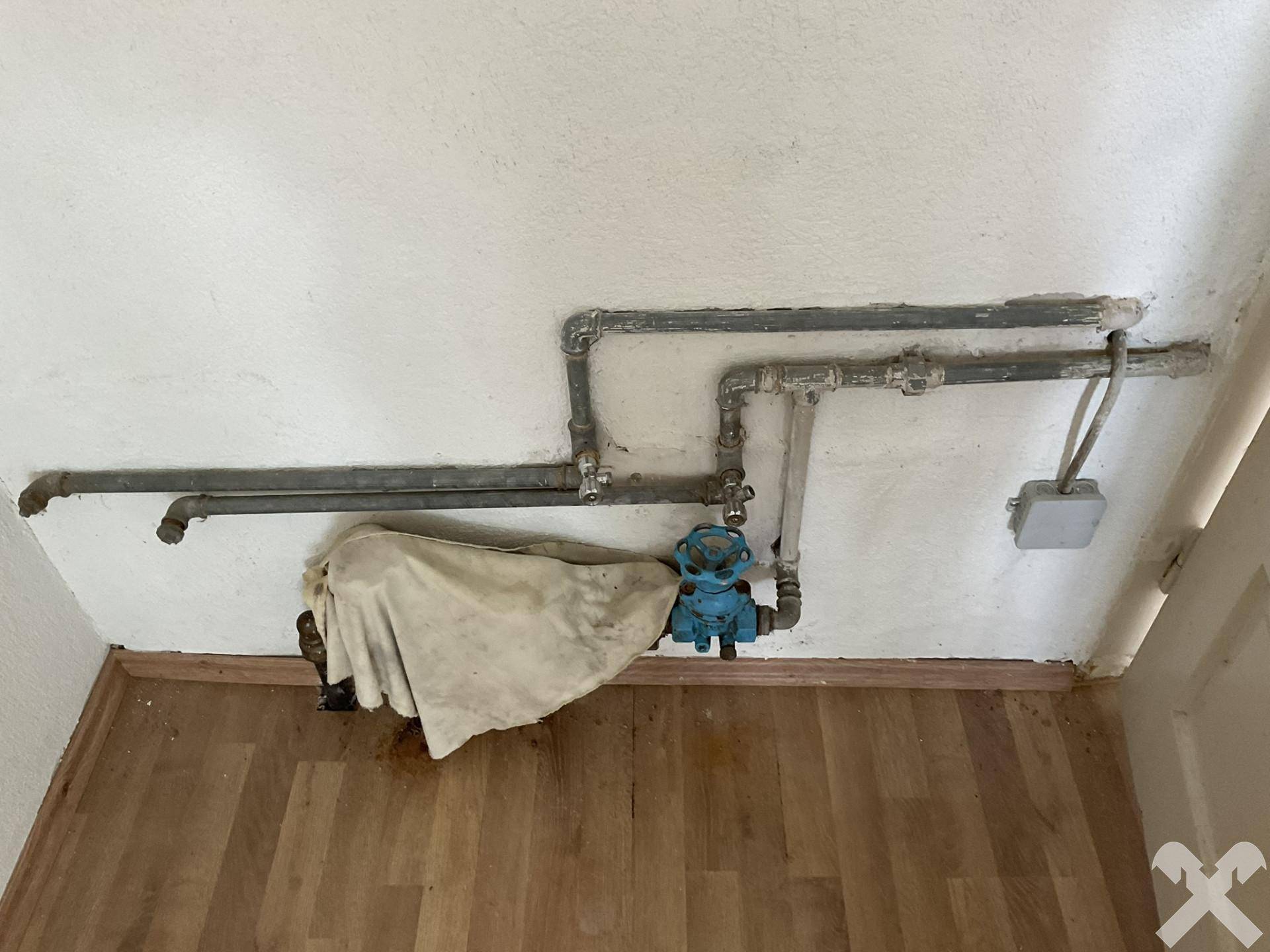Wandbereich mit sichtbaren Wasserleitungen und einem Ventil, deutet auf einen Technik- oder Hauswirtschaftsraum hin.