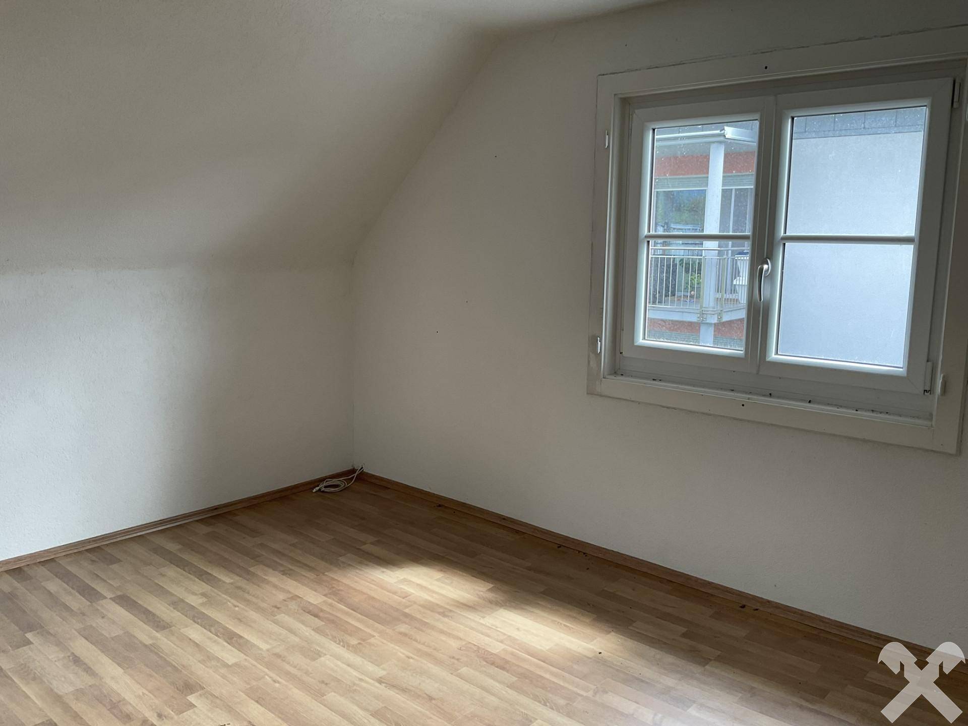 Dachzimmer mit Laminatboden und einem Fenster, das für ausreichend Belichtung sorgt, ideal als Schlafzimmer.