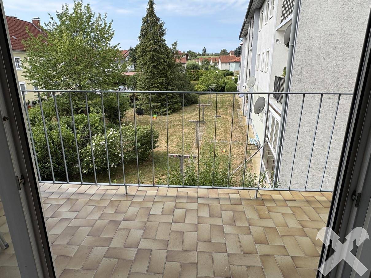 Balkon mit Fliesenboden und Blick auf den Gemeinschaftsgarten und umliegende Häuser.
