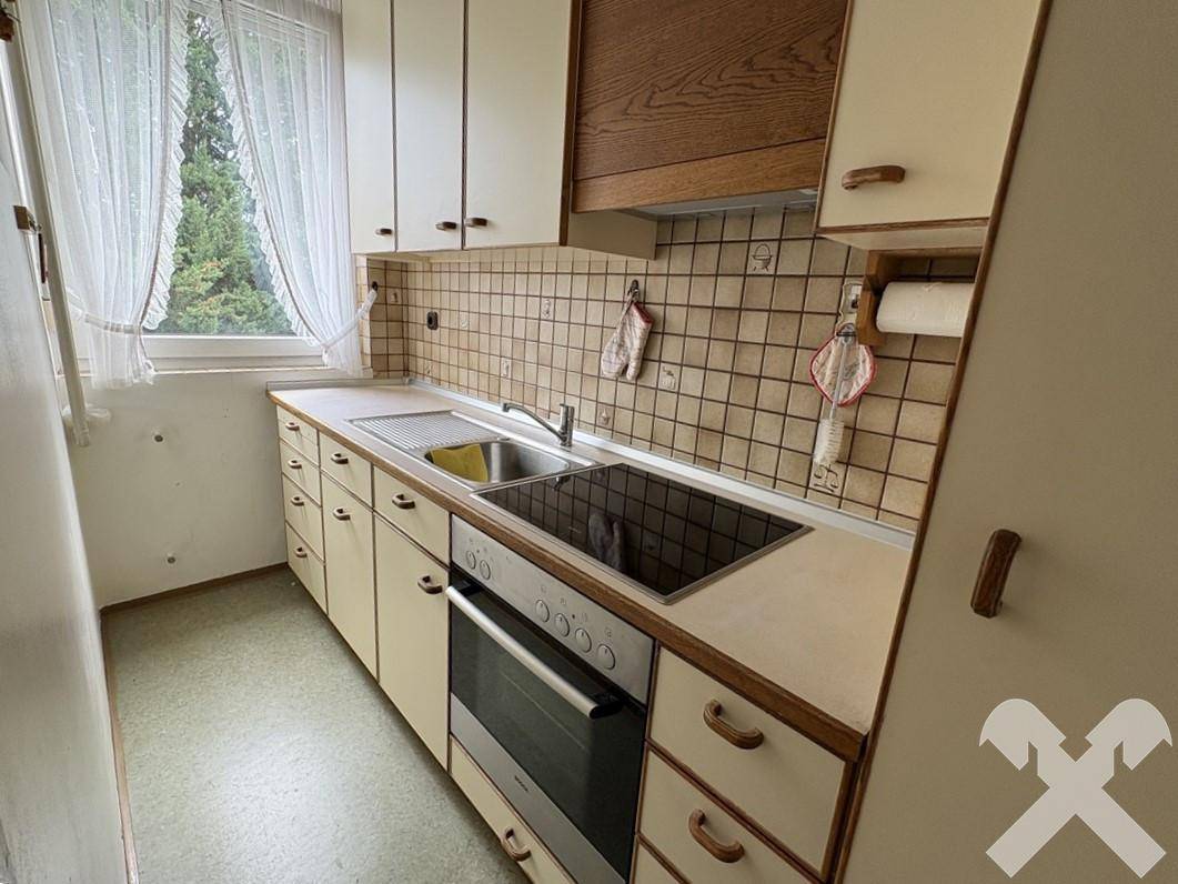 Funktionale Küche mit beigen Fronten, Fliesenrückwand und Fenster mit Blick ins Grüne.