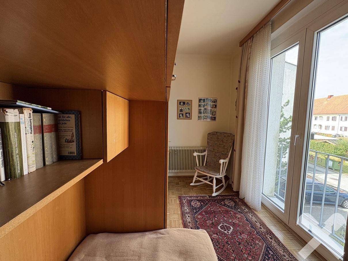 Helles Schlafzimmer mit Parkettboden, Schrankwand und Fenster mit Blick nach draußen.
