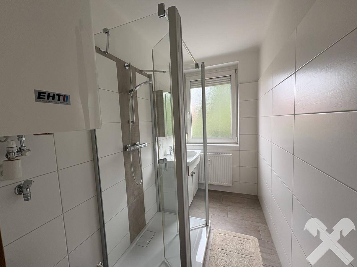Modernisiertes Badezimmer mit ebenerdiger Dusche, weißen Fliesen und Fenster.
