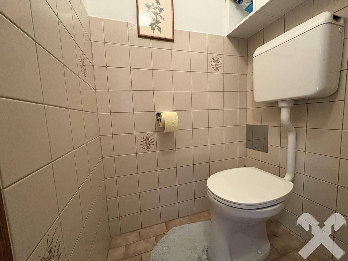 Separate Toilette mit beigen Fliesen und traditionellem Spülkasten.