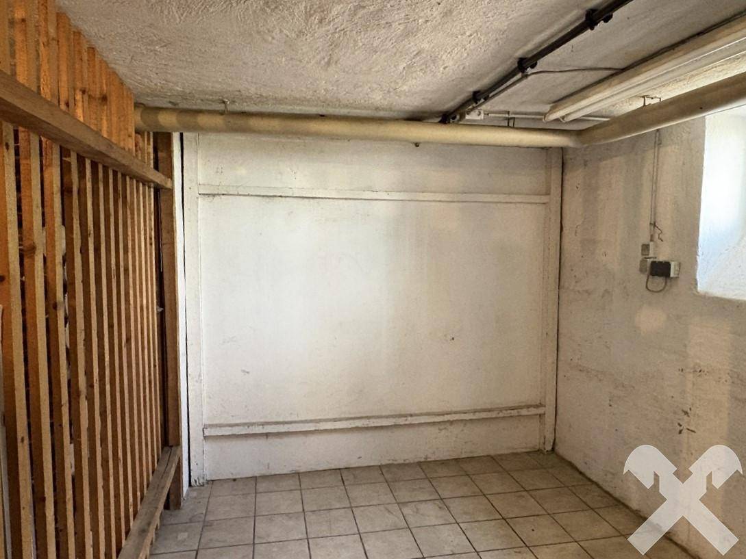 Kellerraum mit Fliesenboden, Holzabtrennung und sichtbaren Leitungen an der Decke.