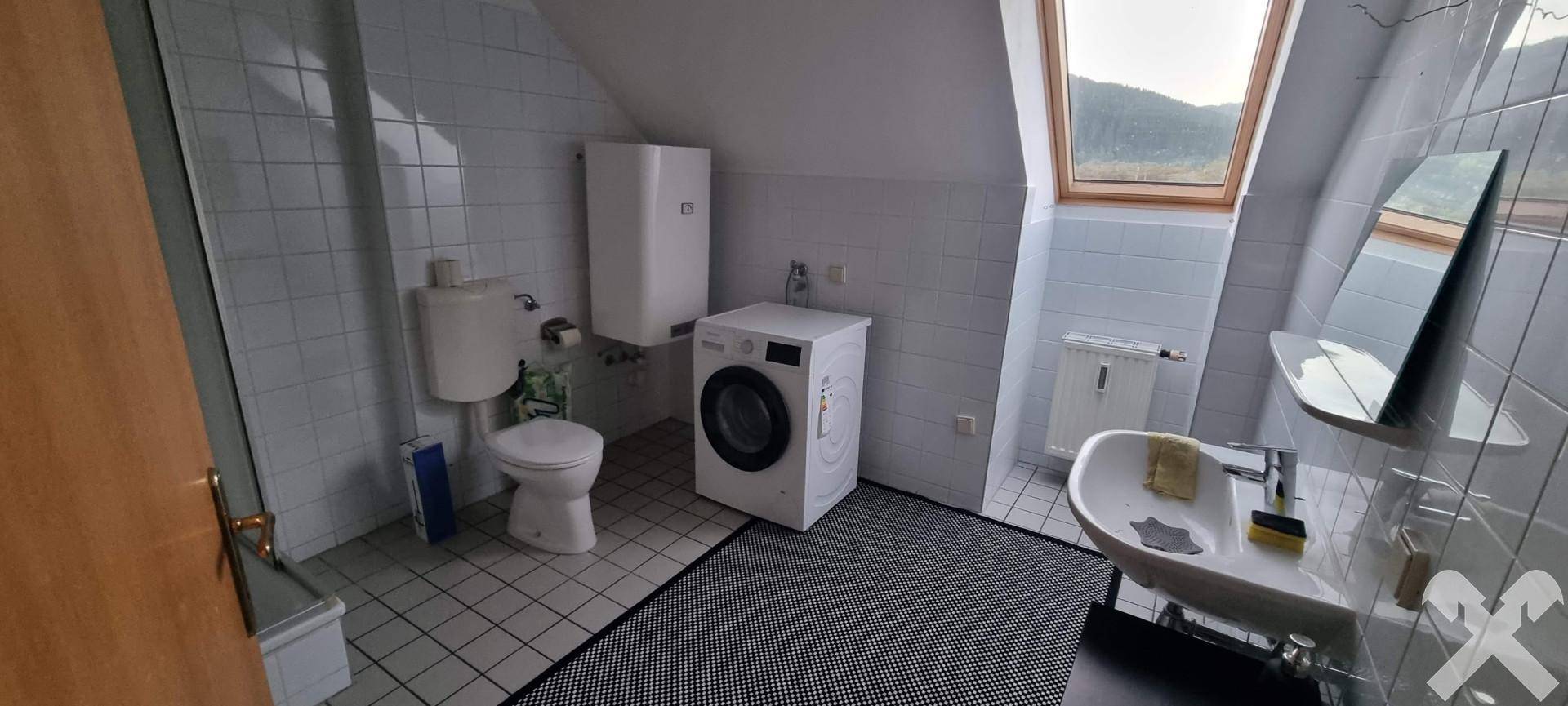 Gefliestes Badezimmer mit Toilette, Waschbecken, Waschmaschine und Dachfenster für natürliches Licht.