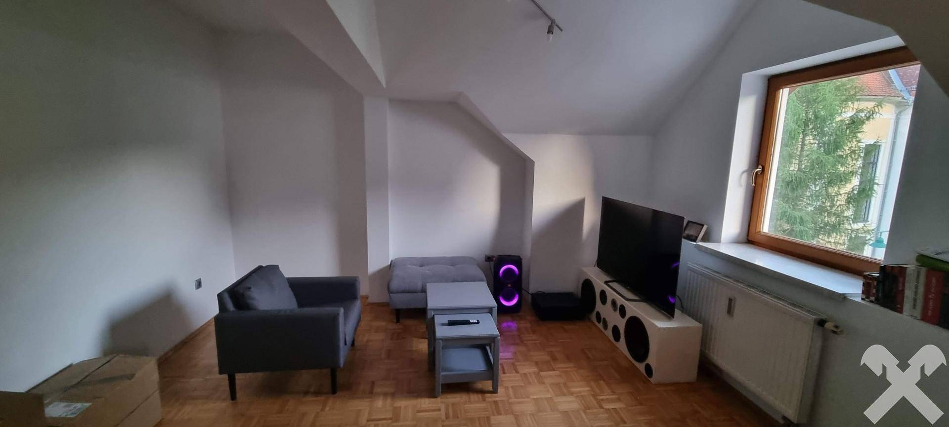 Gemütliches Wohnzimmer mit Parkettboden, Dachschrägen und Blick ins Grüne durch das Fenster.