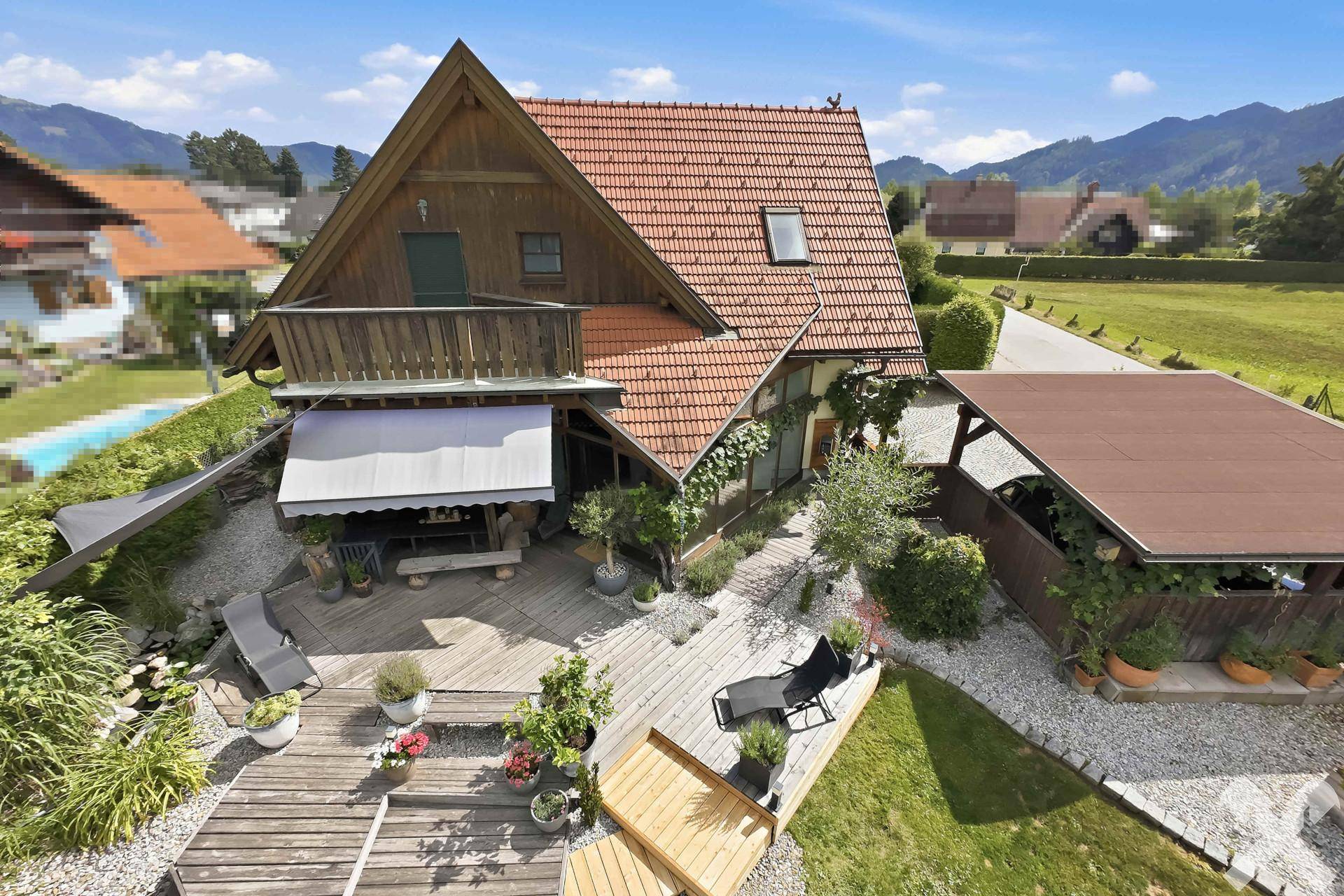 Vogelperspektive des Hauses mit Satteldach, Balkon, großer Holzterrasse und Garten mit Pool.