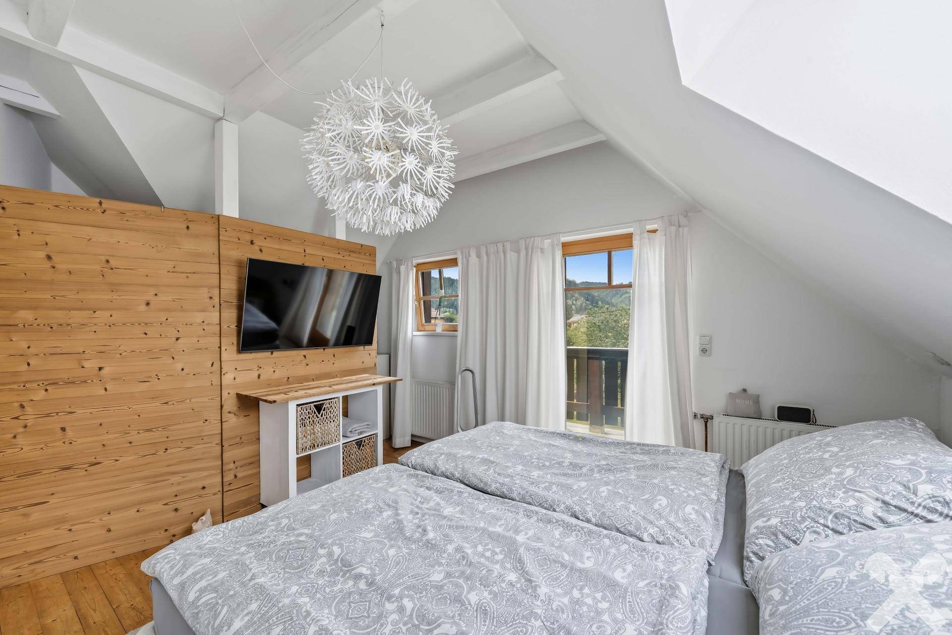 Helles Schlafzimmer mit Holzwand, Doppelbett und Zugang zu einem kleinen Balkon.