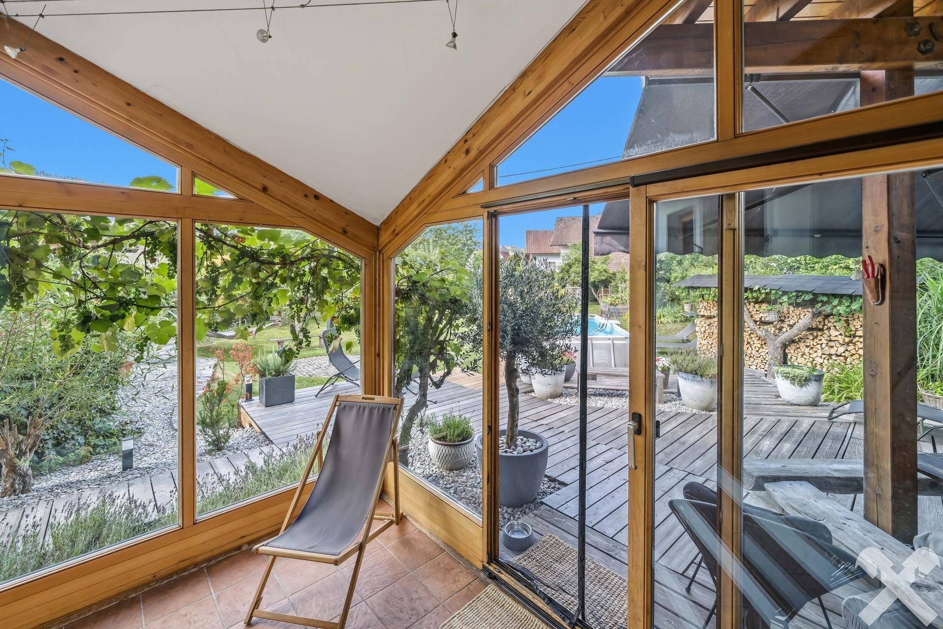 Heller Wintergarten mit großen Glasflächen, Holzbalken und Blick auf die Terrasse und den Garten.