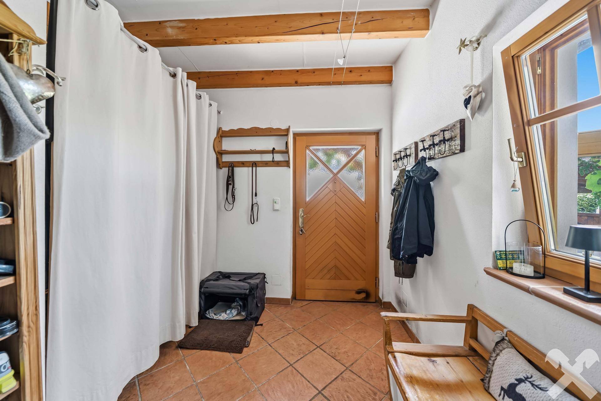 Gemütlicher Eingangsbereich mit Holztür, Garderobe und rustikalen Holzbalken an der Decke.
