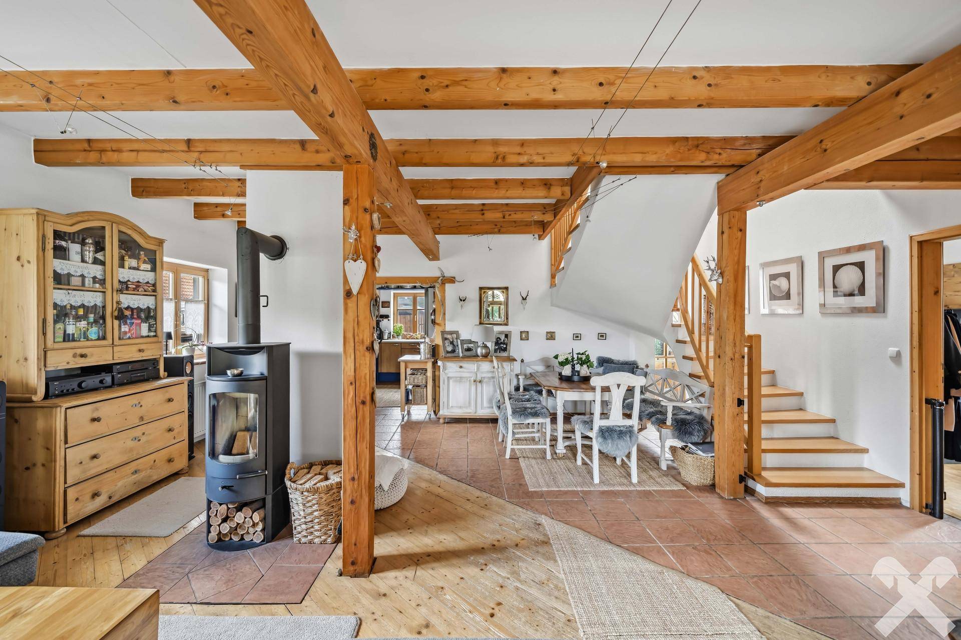 Geräumiger Wohn- und Essbereich mit Kaminofen, Holzbalken und offener Treppe.