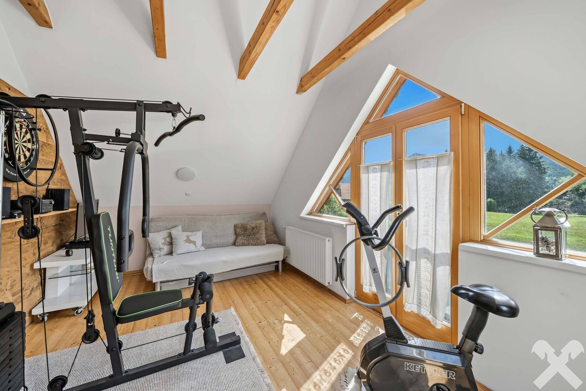 Fitnessraum im Dachgeschoss mit Trainingsgeräten, Sofa und großen Fenstern mit Ausblick.