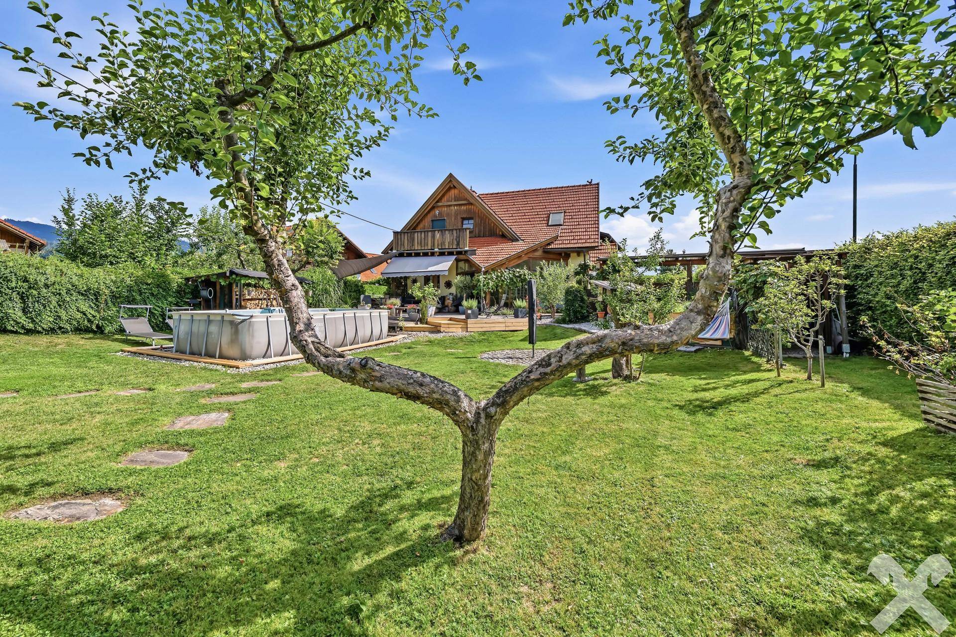 Großer Garten mit Rasenfläche, Obstbäumen, einem Aufstellpool und einer Holzterrasse vor dem Haus.