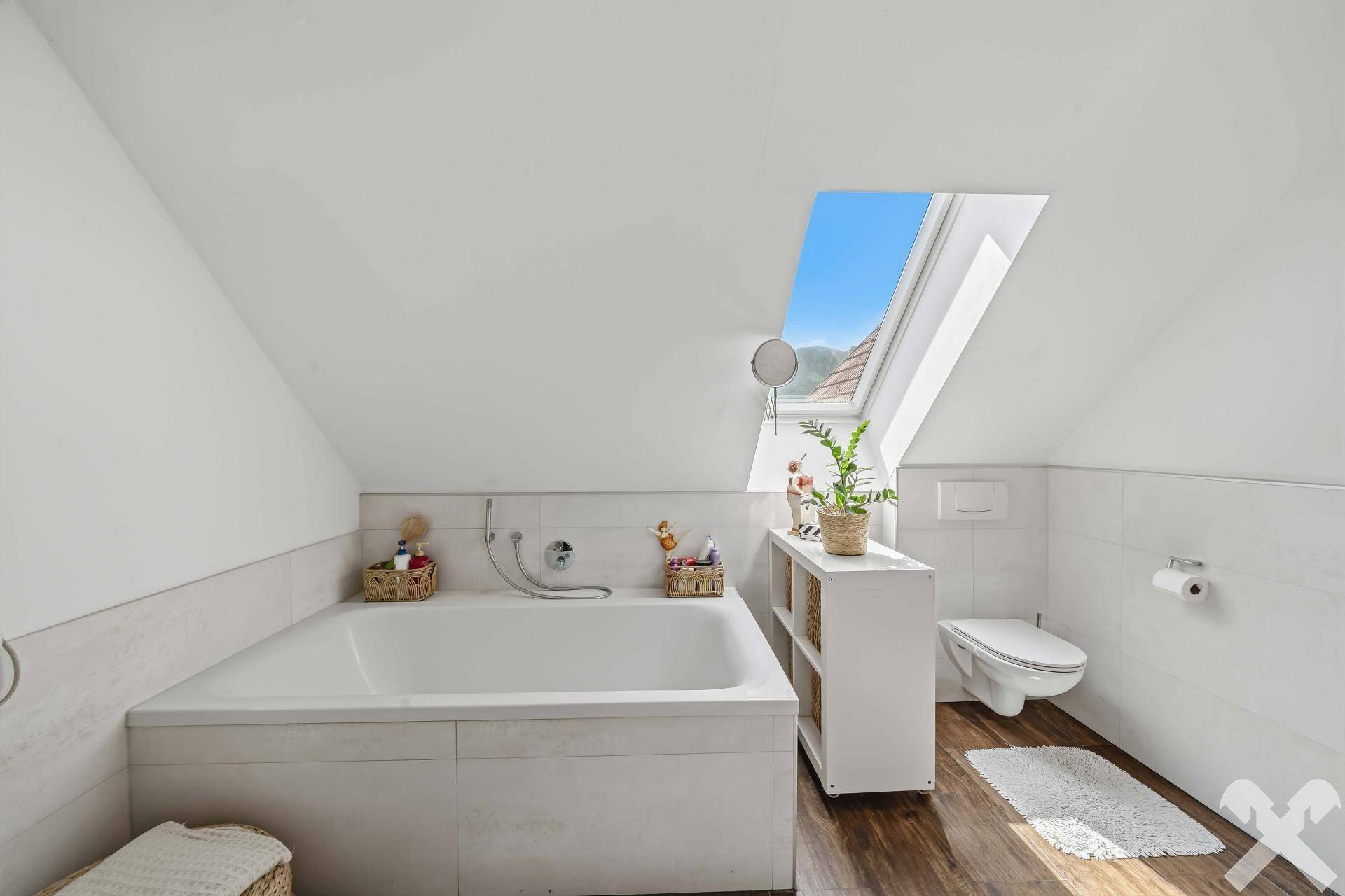 Helles Badezimmer mit Badewanne, wandhängendem WC und Dachfenster für viel Tageslicht.