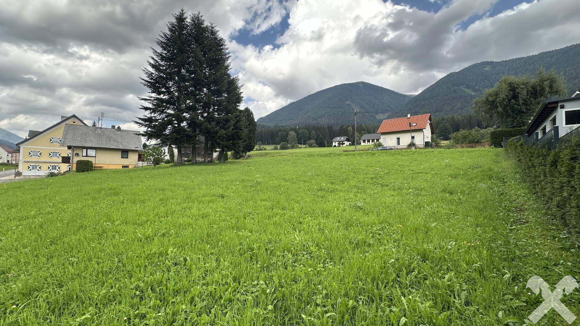 Offene Grünfläche mit Blick auf die umliegende Bebauung und die Alpen unter einem bewölkten Himmel.