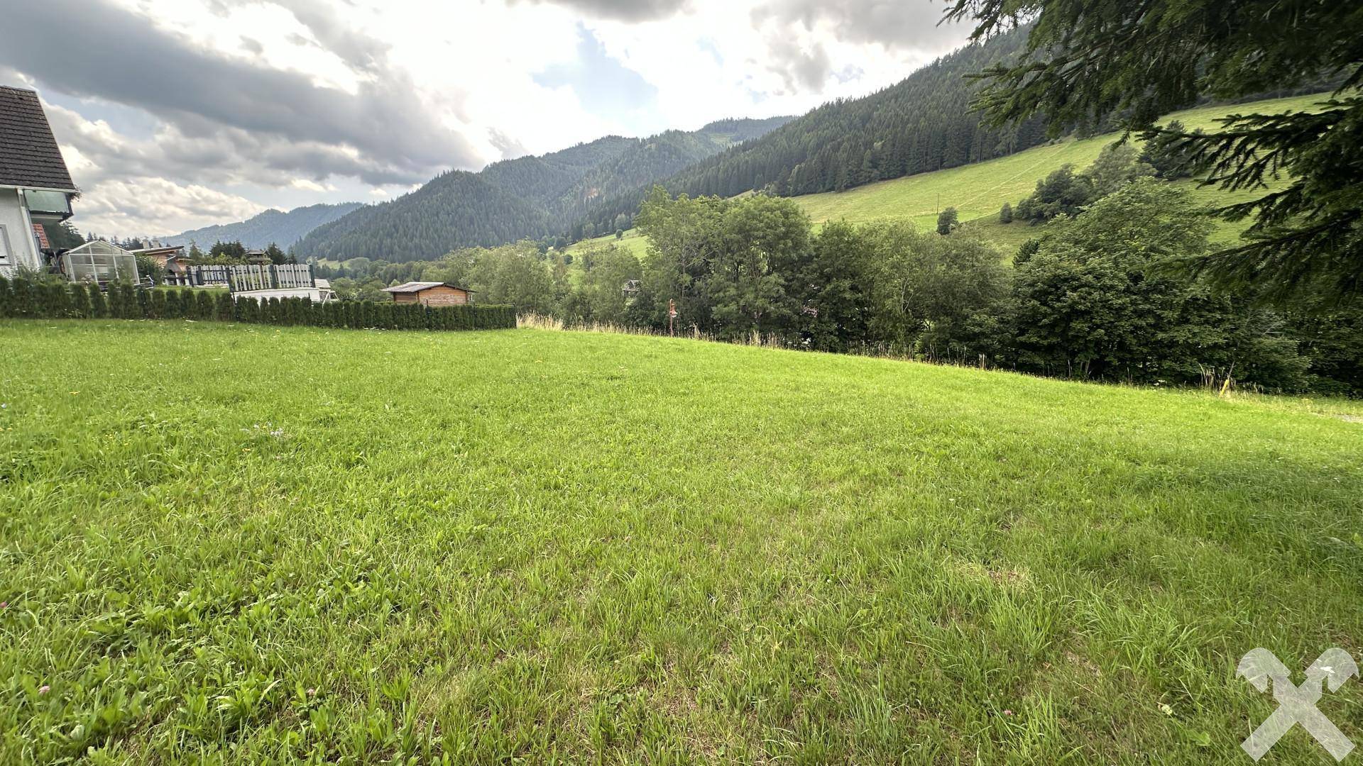 Weitläufige grüne Fläche mit Blick auf die bewaldeten Hügel und angrenzende Häuser in der Ferne.