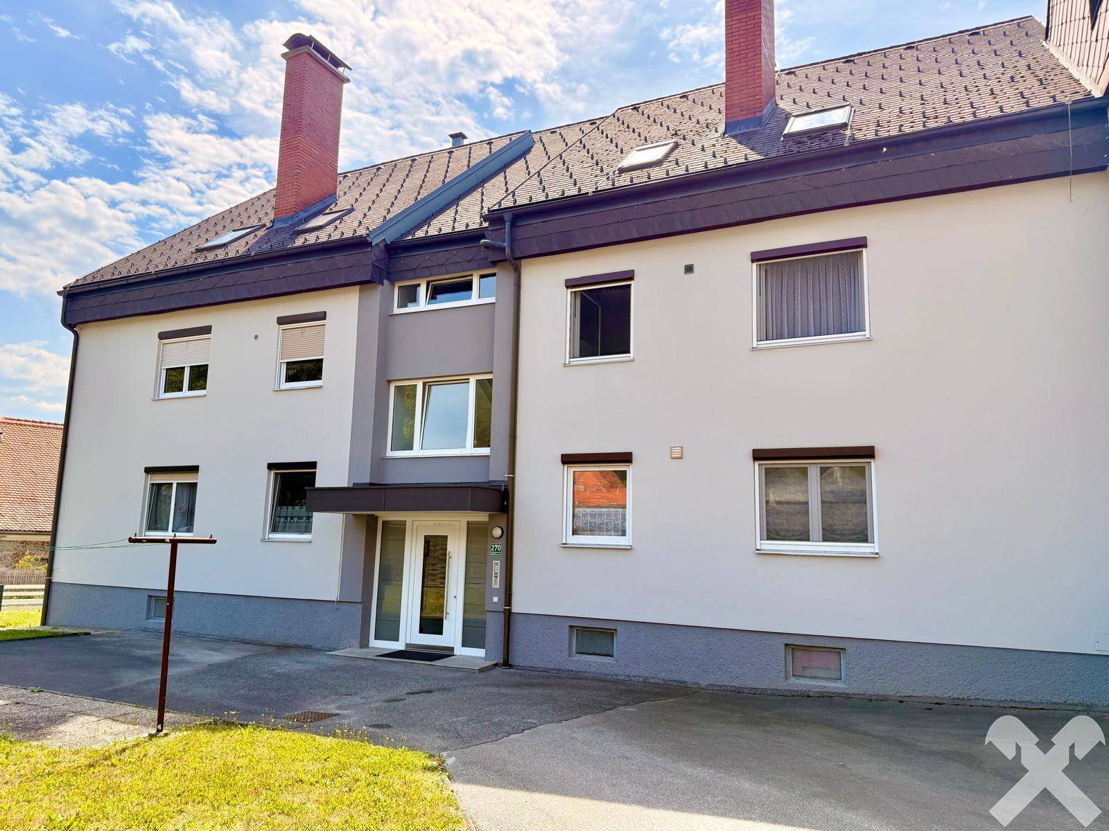 Vorderansicht des Wohngebäudes mit Eingangsbereich, Fenstern und gepflegter Fassade an einem sonnigen Tag.