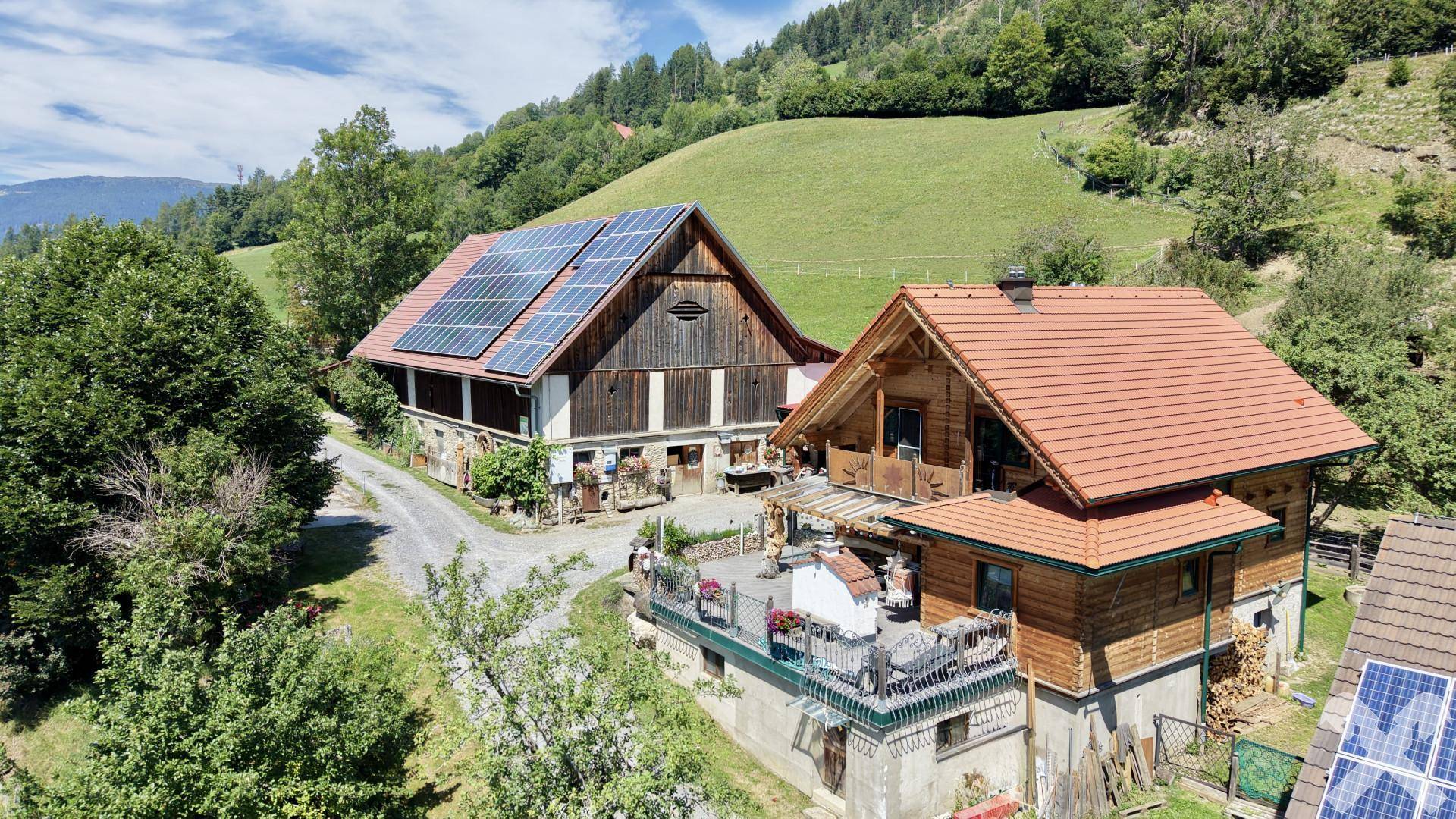 Ländliches Anwesen mit mehreren Gebäuden, Solarpaneelen auf den Dächern und einer Terrasse.