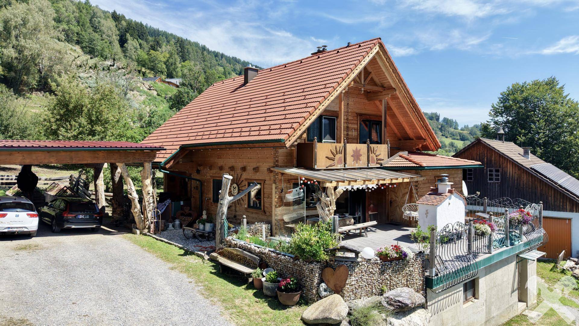 Charmantes Holzhaus mit großzügiger Terrasse, Carport und traditioneller Architektur in ländlicher Umgebung.