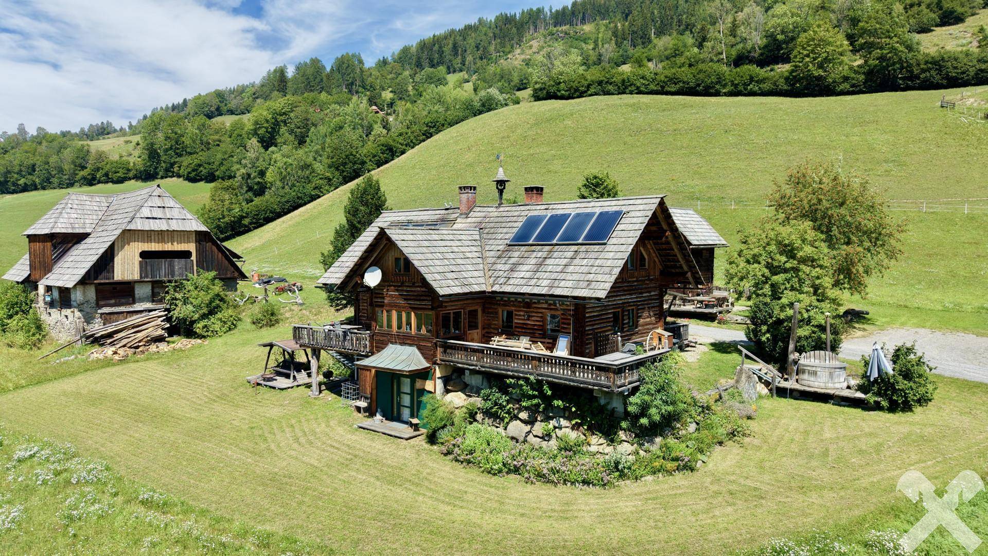 Rustikales Holzhaus mit Holzdach und Solarpaneelen, eingebettet in eine idyllische Berglandschaft.